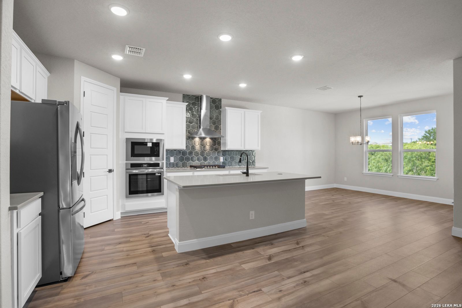 Modern kitchen with white cabinets, large island, and hexagon tile backsplash in The Jennings G plan, Ladera, San Antonio.