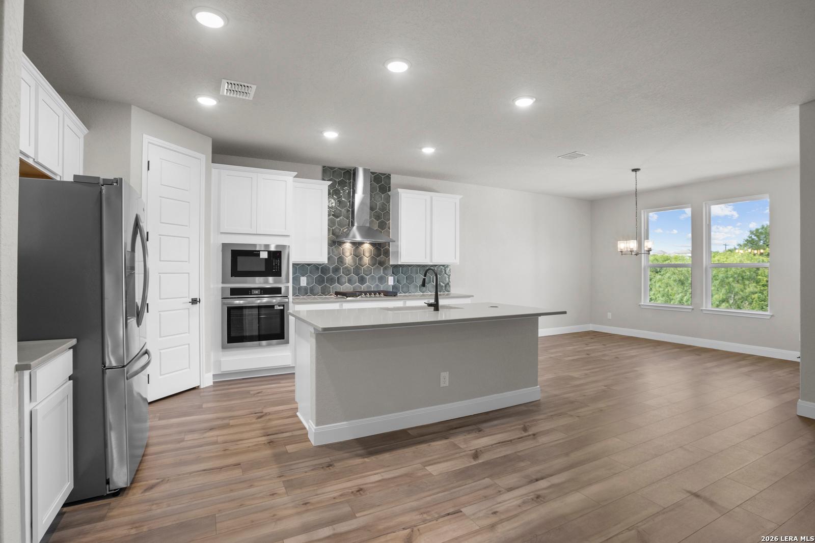 Modern kitchen with white cabinets, large island, and hexagon tile backsplash in The Jennings G plan, Ladera, San Antonio.