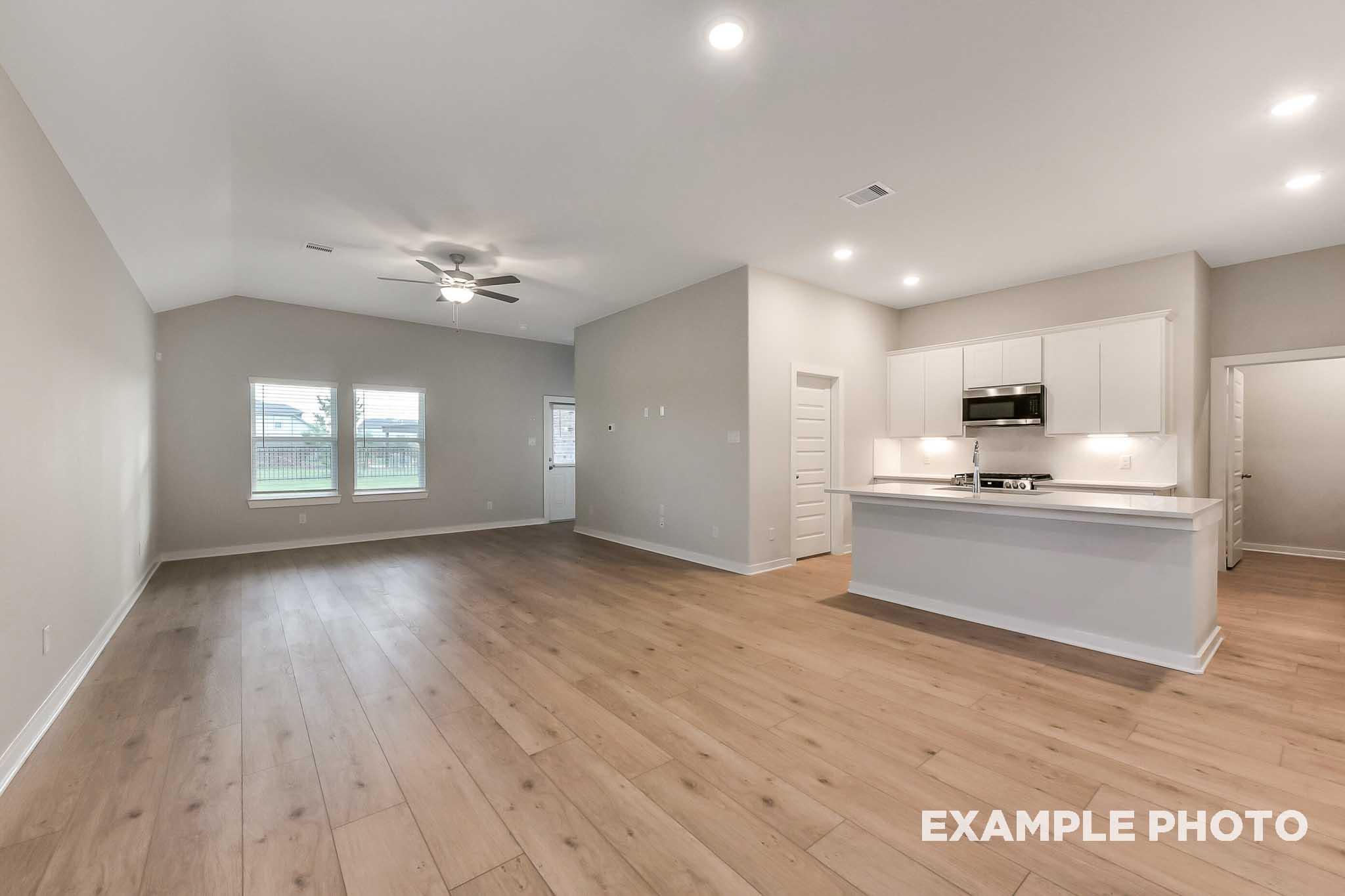 Spacious open-concept living kitchen in The Laguna B featuring hardwood floors, ceiling fan, white island cabinets, and large windows