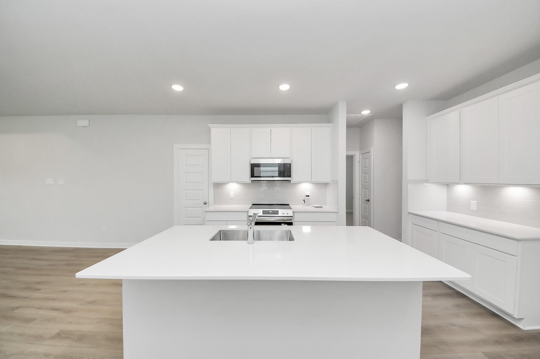 Modern white kitchen island with stainless sink and quartz countertops in The Frio F floor plan, Liberty Estates, Texas.