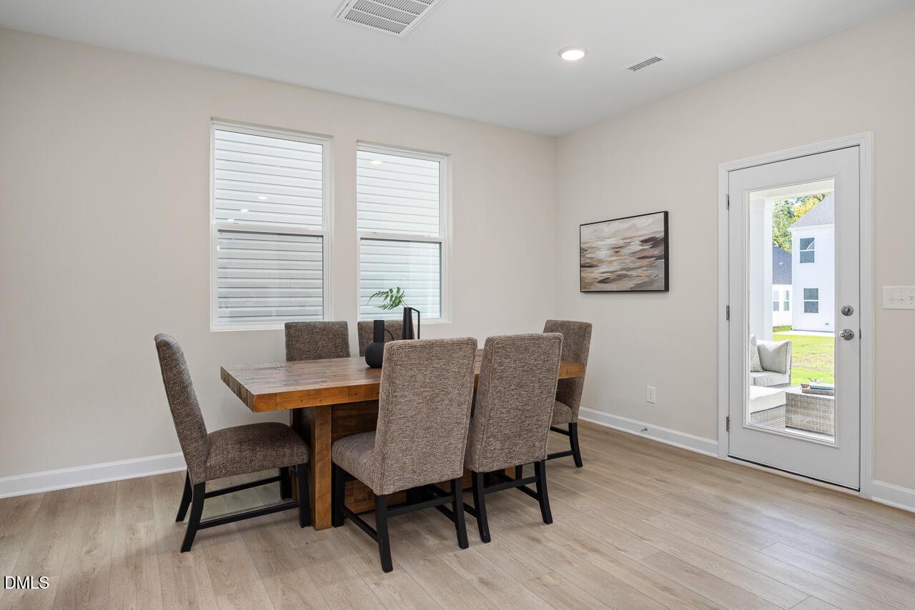 Modern dining room with wooden table, upholstered chairs, and glass door to backyard patio in Davidson Homes Preston A, Lillington, NC