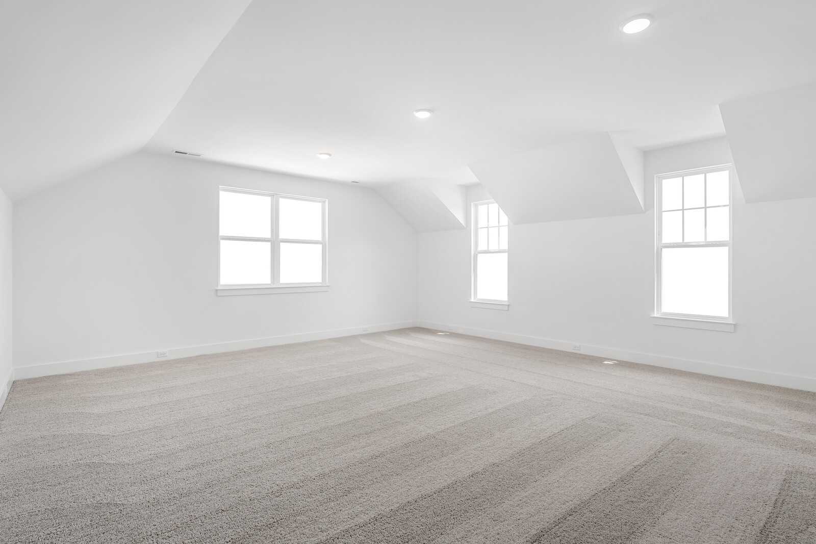 Spacious empty bonus room with vaulted ceiling, double windows, and beige carpet in Davidson Homes The Hathaway, Murfreesboro