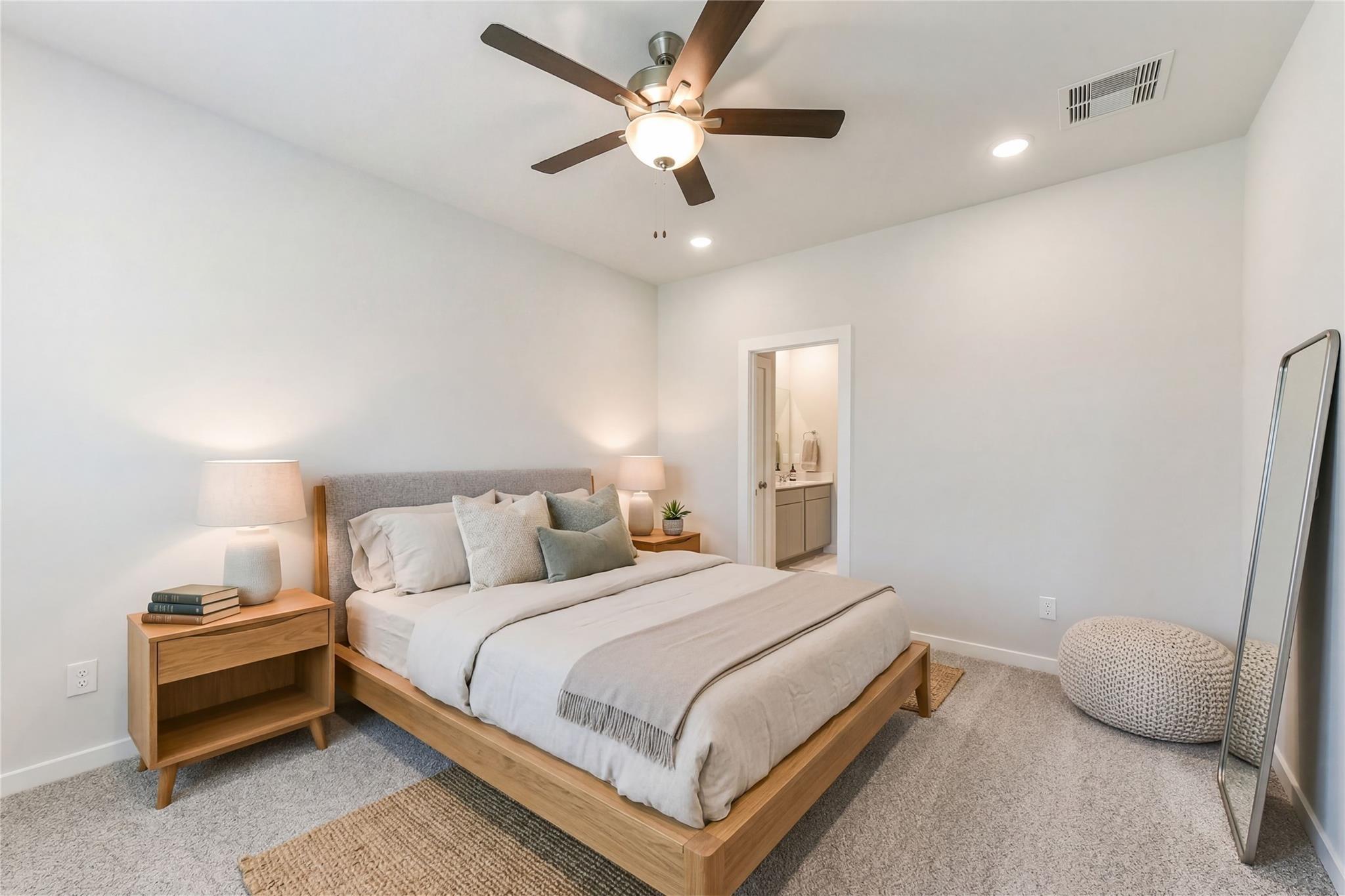 Bright bedroom with wooden platform bed, neutral linens, ceiling fan, and en-suite bath in Davidson Homes Brazos E, Magnolia TX