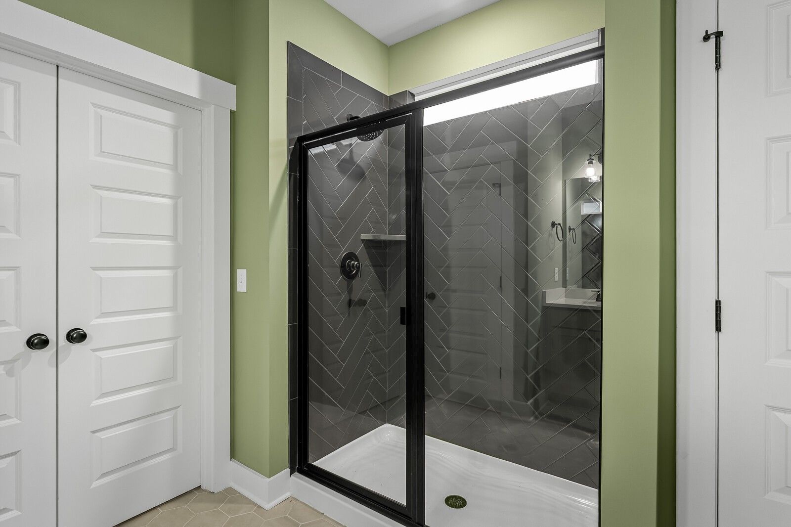 Contemporary bathroom with frameless glass shower, black herringbone tiles, and green accent wall in Davidson Homes Ridgeport, Gallatin TN