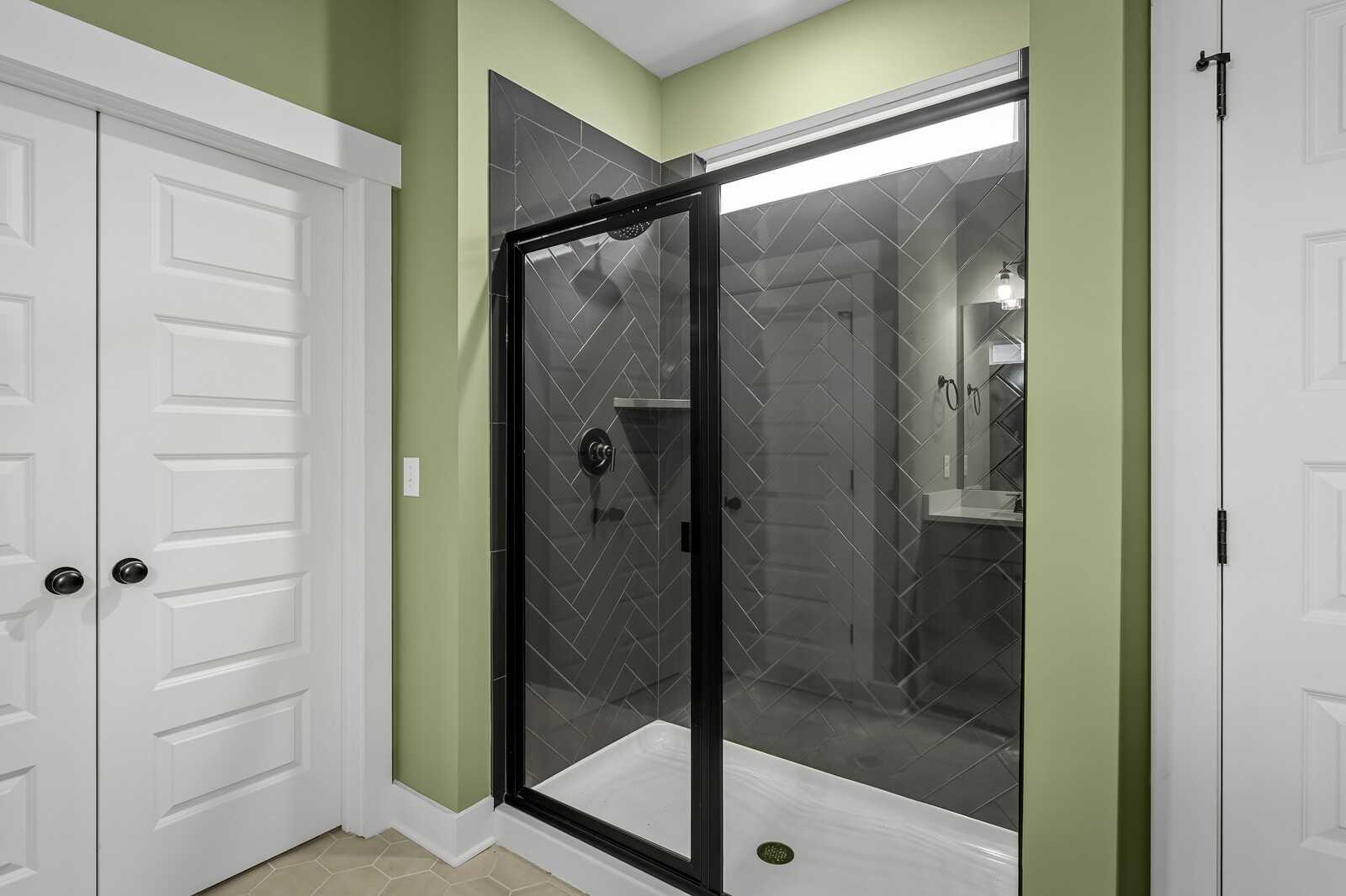 Contemporary bathroom with frameless glass shower, black herringbone tiles, and green accent wall in Davidson Homes Ridgeport, Gallatin TN