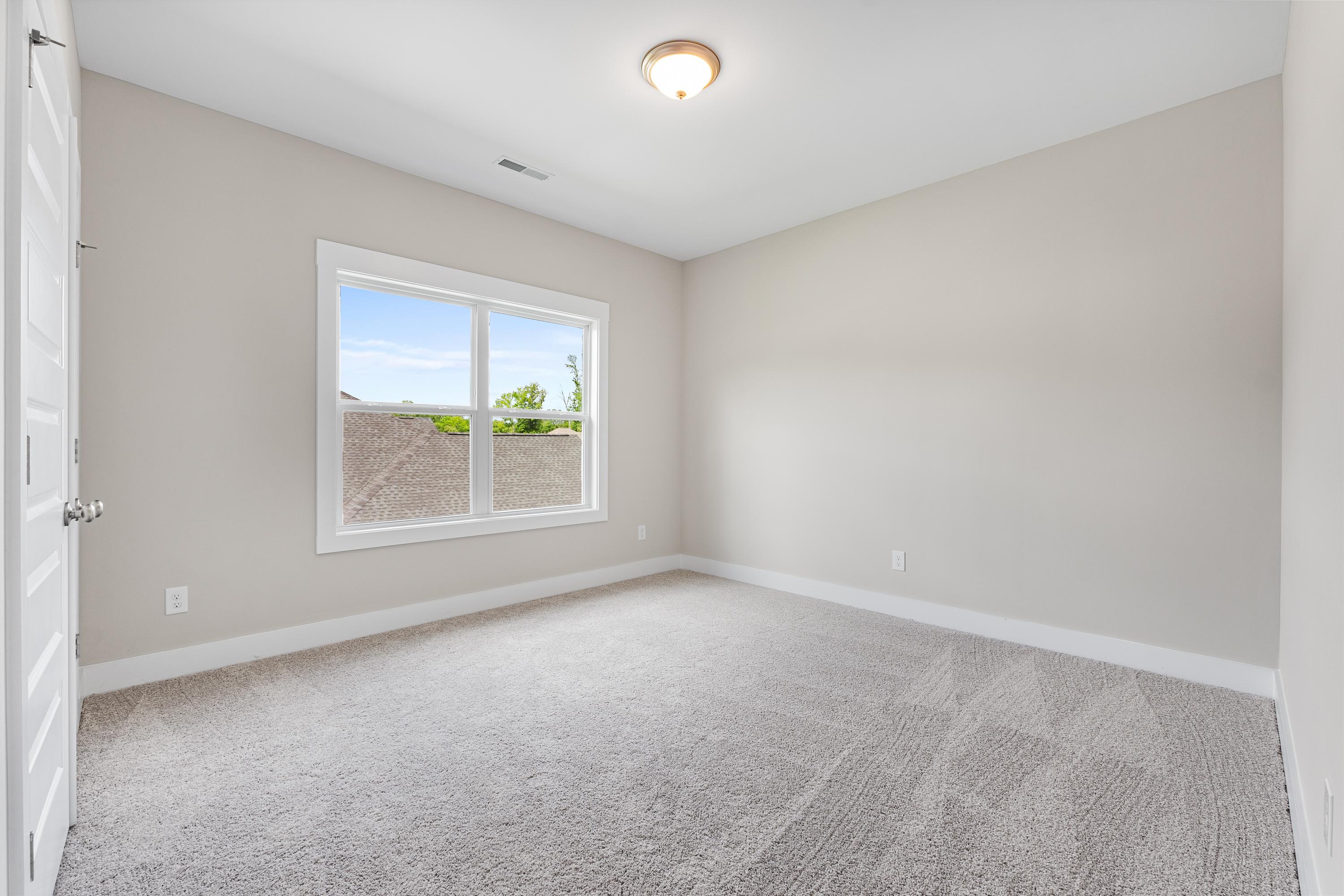 Spacious secondary bedroom in The Oxford A with beige walls, carpeted floor, large window, and ceiling light