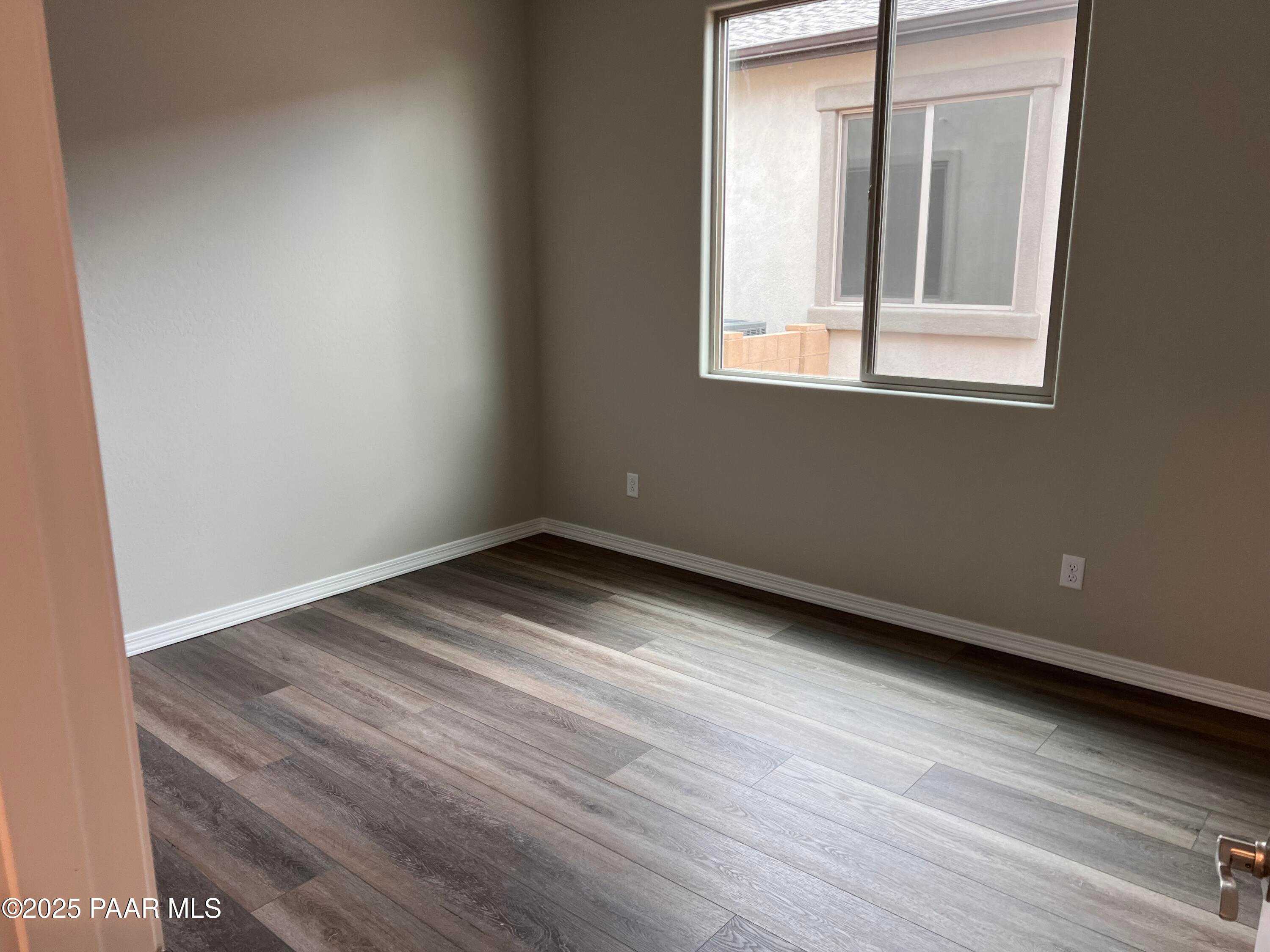 Empty bedroom featuring beige walls, luxury vinyl plank flooring, and large sliding glass window in Davidson Homes The Harmony A, Prescott Valley, AZ