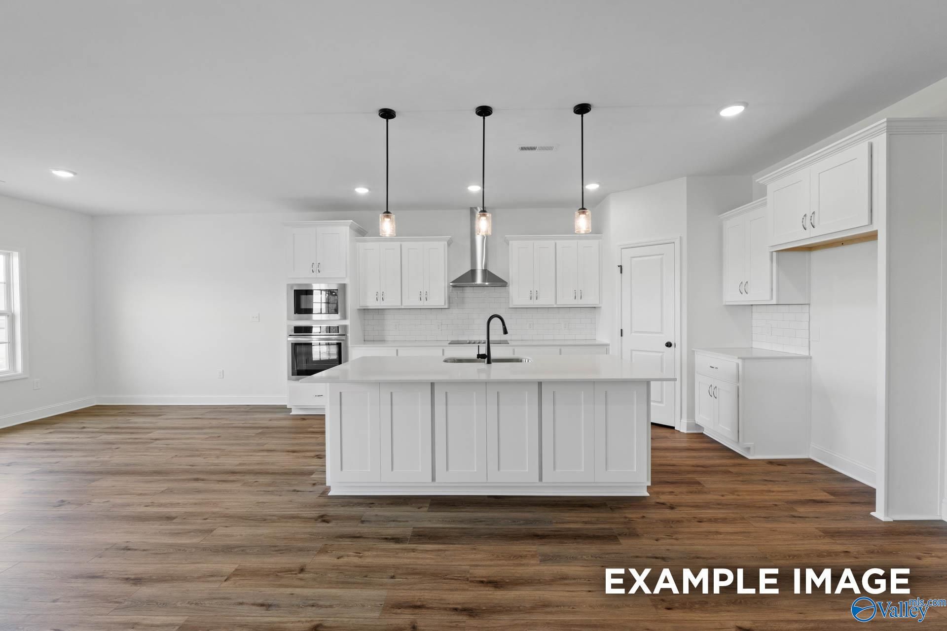 Modern kitchen with white cabinets, large island, and stainless appliances in The Rockford B home at Briercreek, Meridianville.