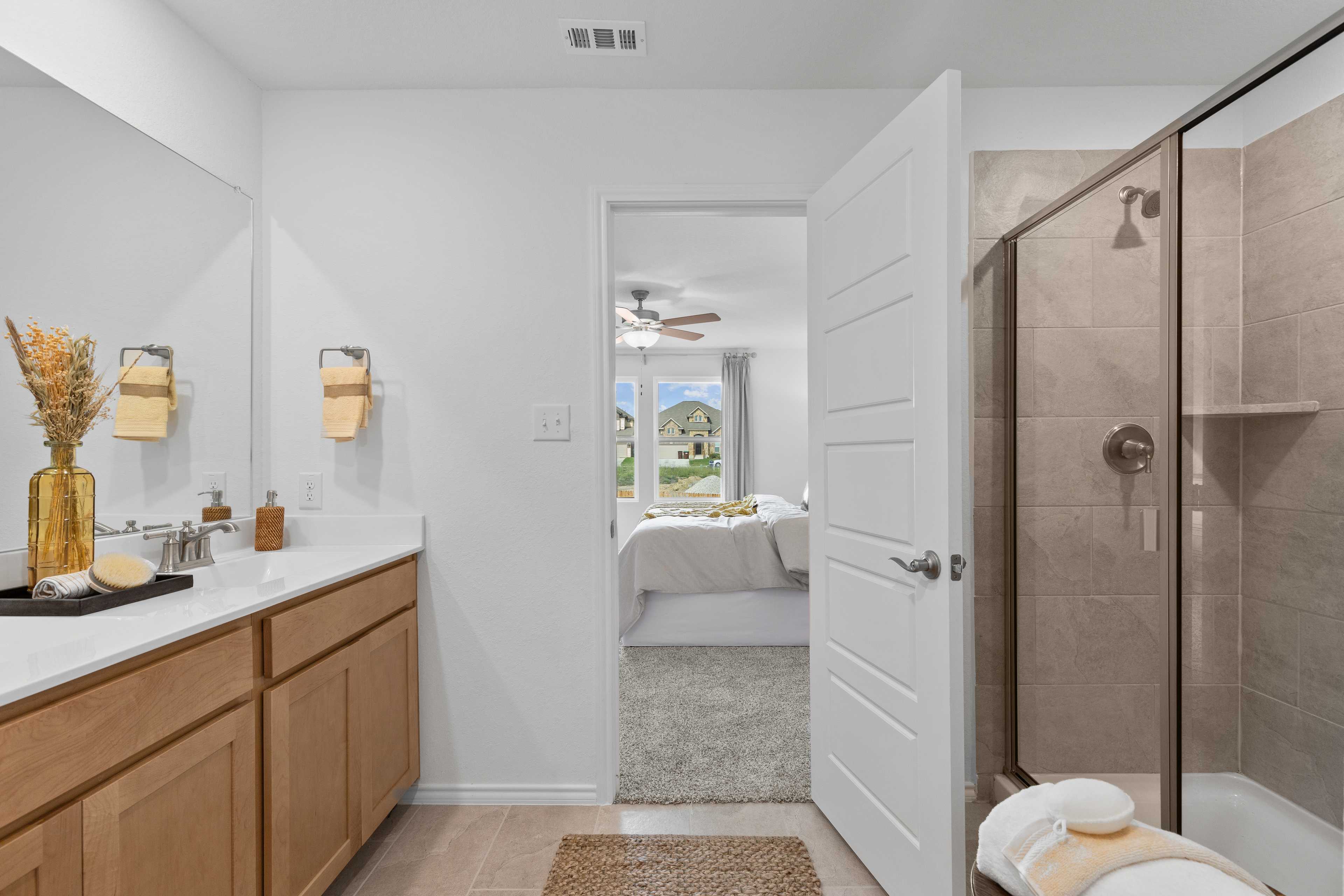 Spacious primary bathroom at Horizon Pointe in Converse TX by Davidson Homes with oak vanity, walk-in shower, and bedroom view