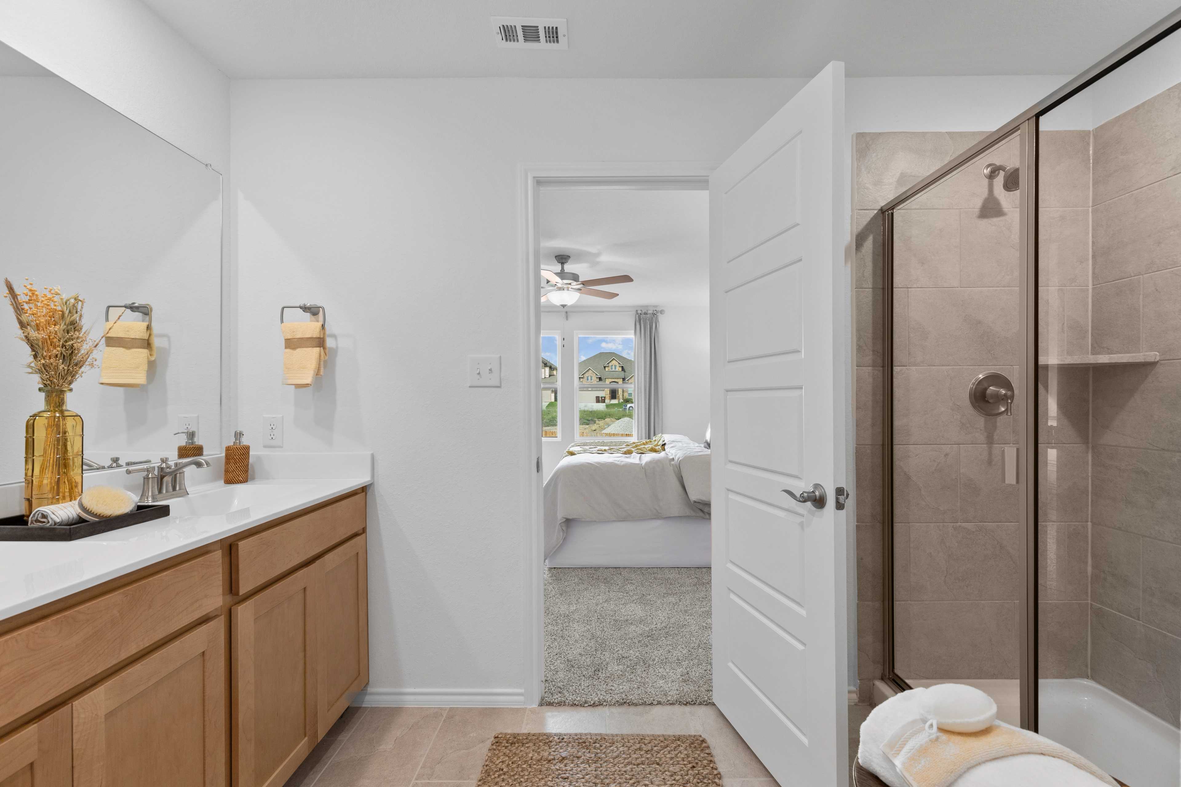 Spacious primary bathroom at Horizon Pointe in Converse TX by Davidson Homes with oak vanity, walk-in shower, and bedroom view