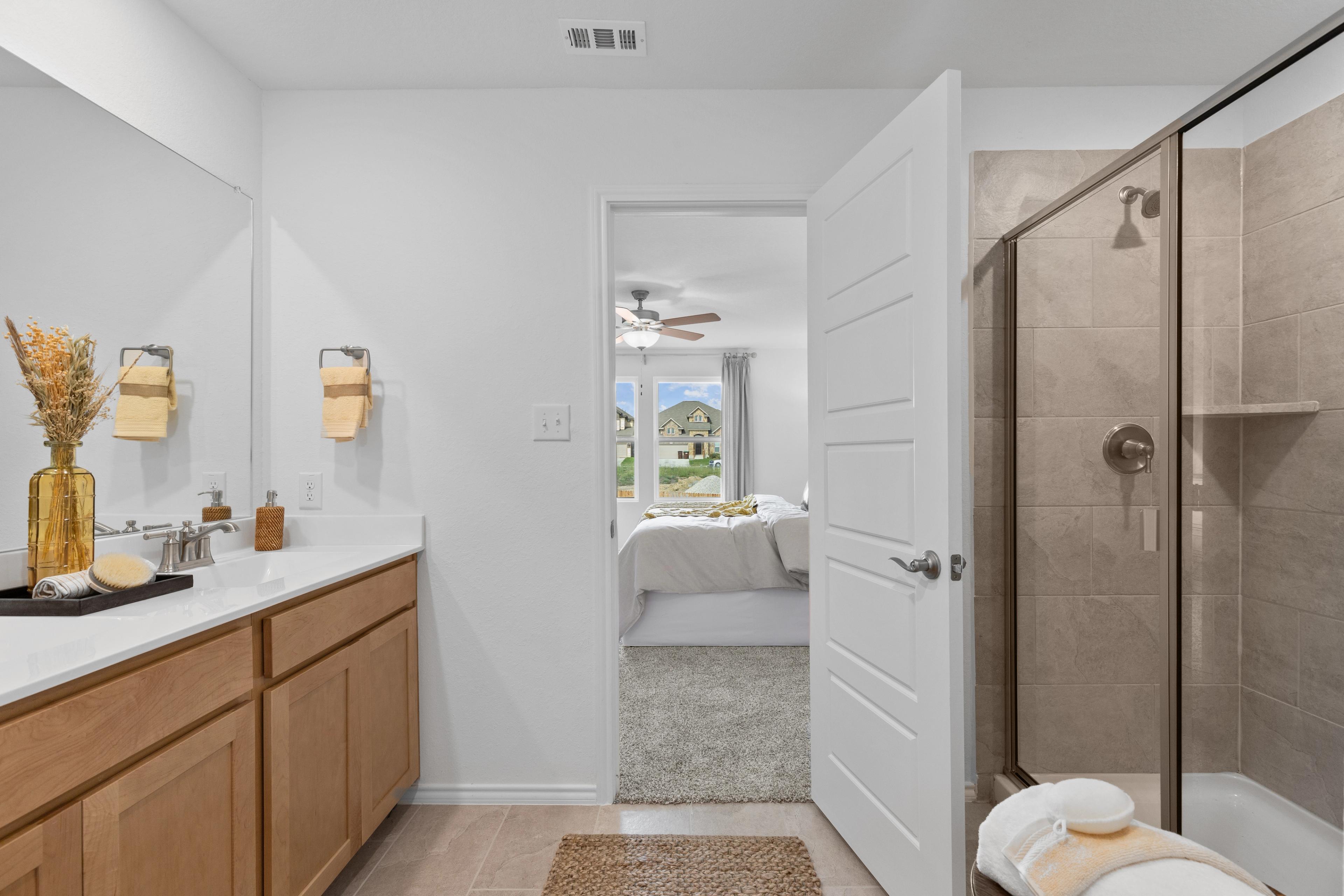 Spacious primary bathroom at Horizon Pointe in Converse TX by Davidson Homes with oak vanity, walk-in shower, and bedroom view