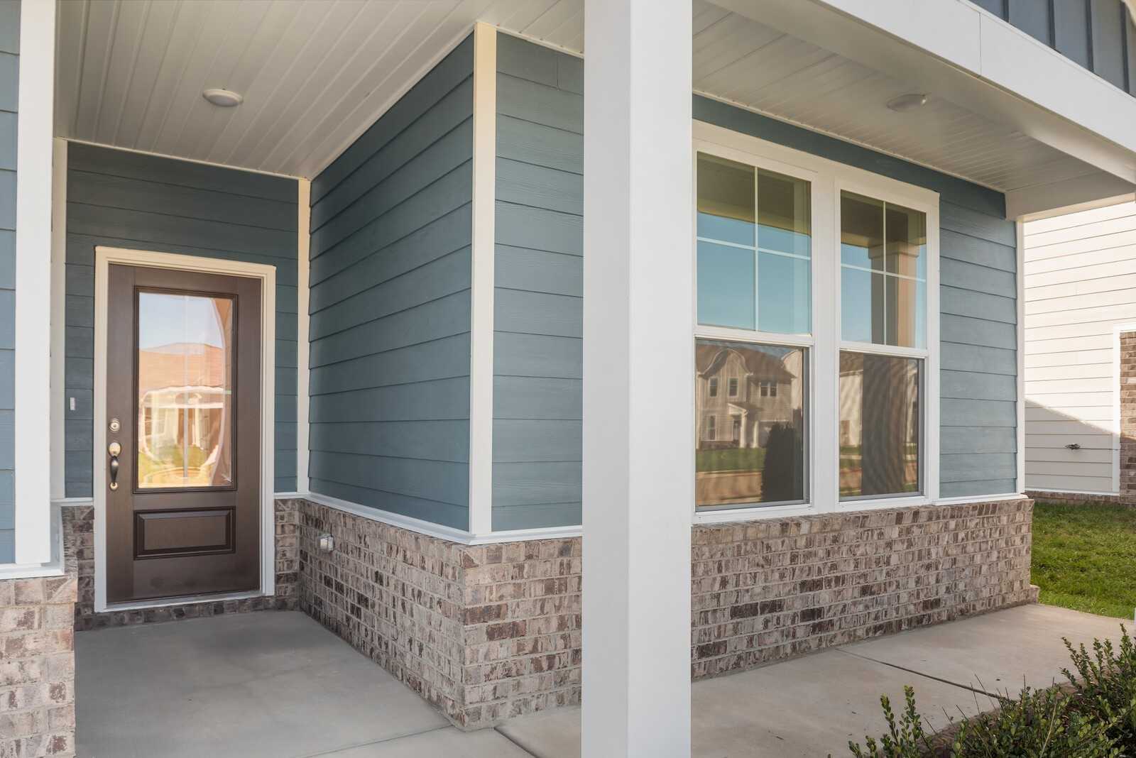 Modern blue board-and-batten exterior with covered porch, glass front door, and brick base in Davidson Homes The Franklin B, Sage Farms, White House, Tennessee
