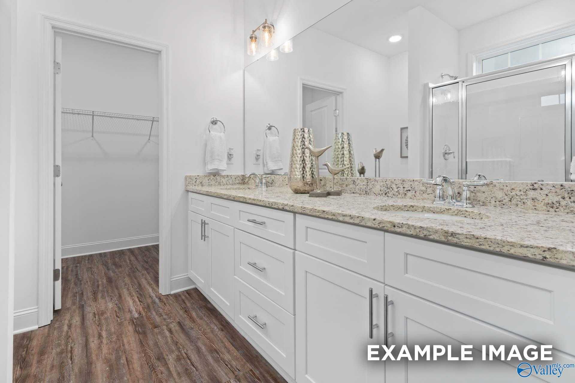 Elegant master bathroom with double granite vanity, white cabinets, frameless shower, and walk-in closet in Davidson Homes Cumberland B, Decatur AL