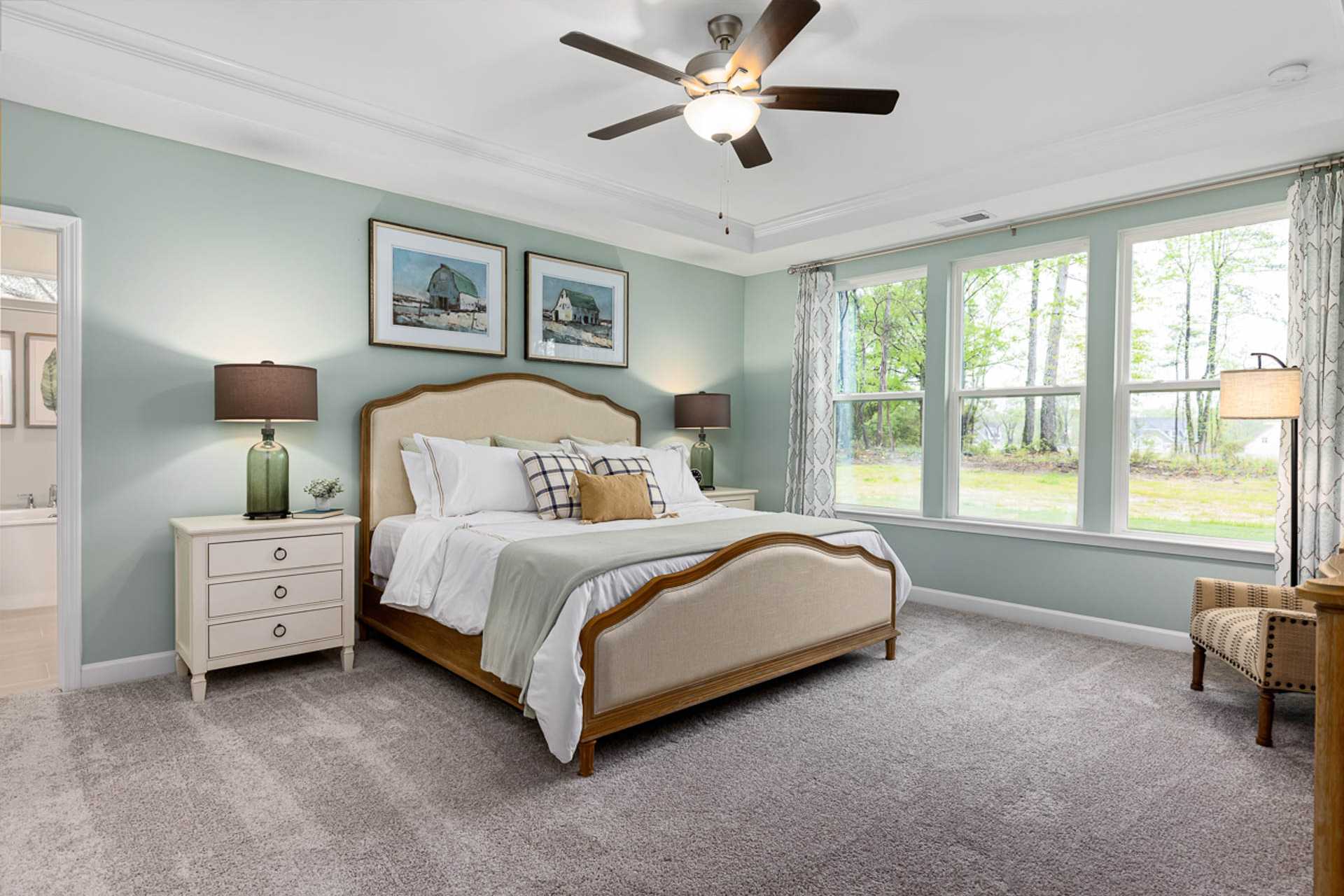 Spacious master bedroom at Weatherford East in Angier NC with tufted king bed, ceiling fan, and large wooded-view windows