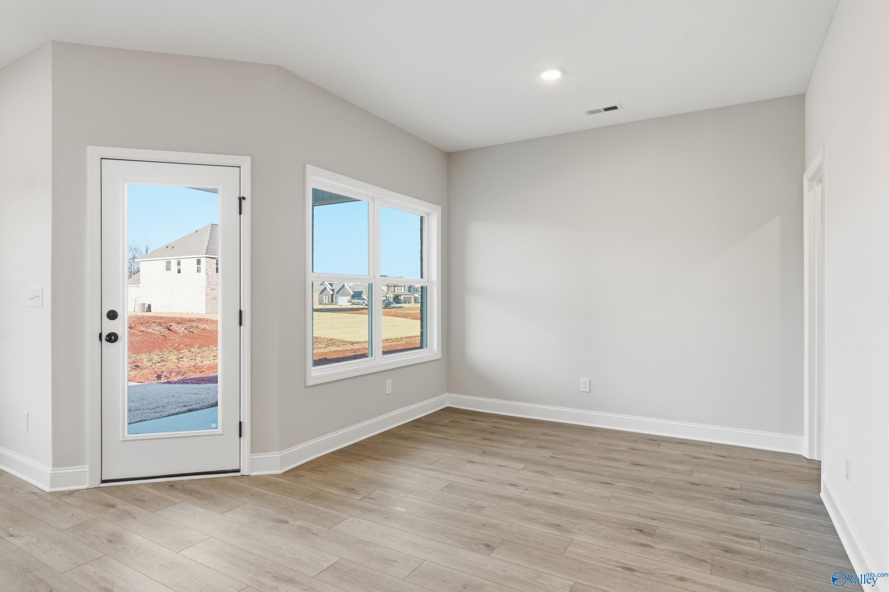 Bright empty room with light gray walls, hardwood floors, large window, and white doors in Davidson Homes The Daphne C, Athens AL