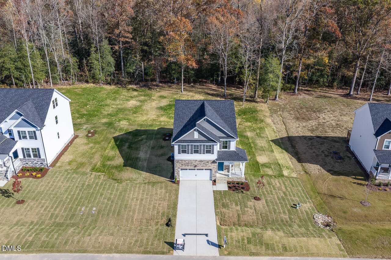 Aerial view of The Gavin C two-story home with stone accents, two-car garage, driveway, and grassy yard amid fall foliage in Wellers Knoll, Lillington, NC
