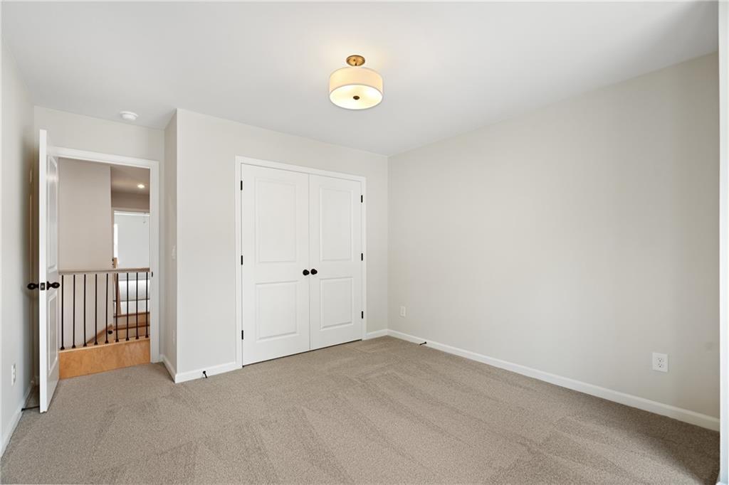 Spacious secondary bedroom with beige carpet, light gray walls, double closet doors, and staircase view in Davidson Homes The Marion A, Kennesaw