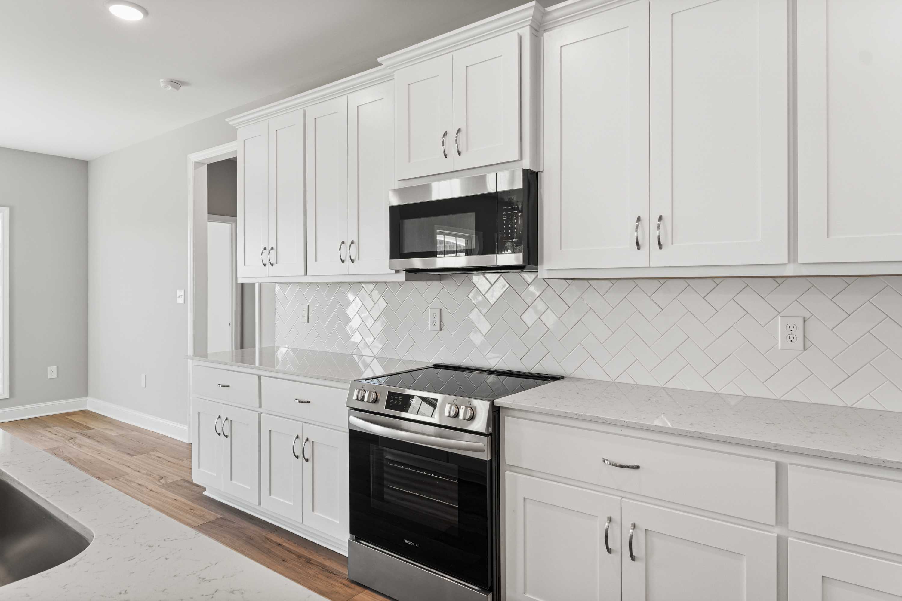 Modern Valencia kitchen featuring white shaker cabinets, herringbone subway tile backsplash, stainless steel appliances, quartz counters