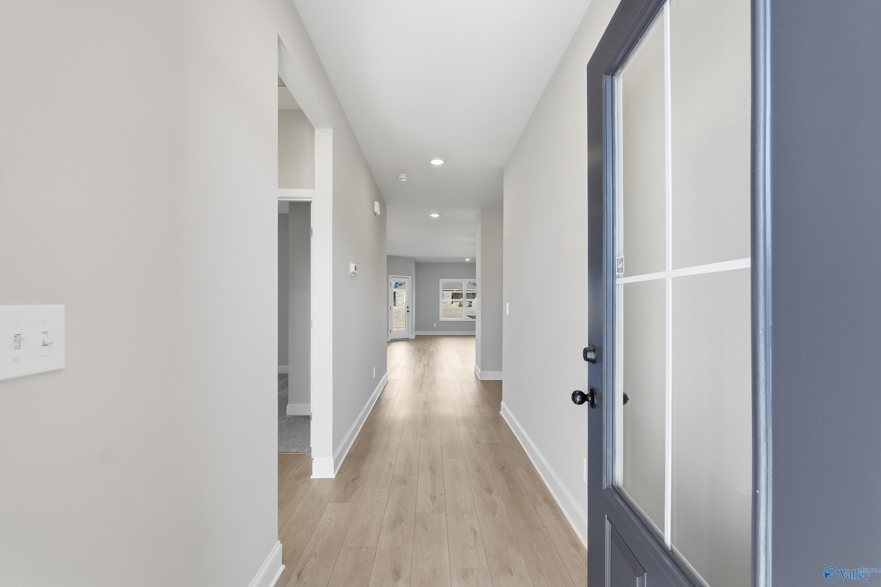 Bright hallway with light oak floors and neutral walls leading to glass-paneled front door in Davidson Homes The Franklin C, New Market, Alabama
