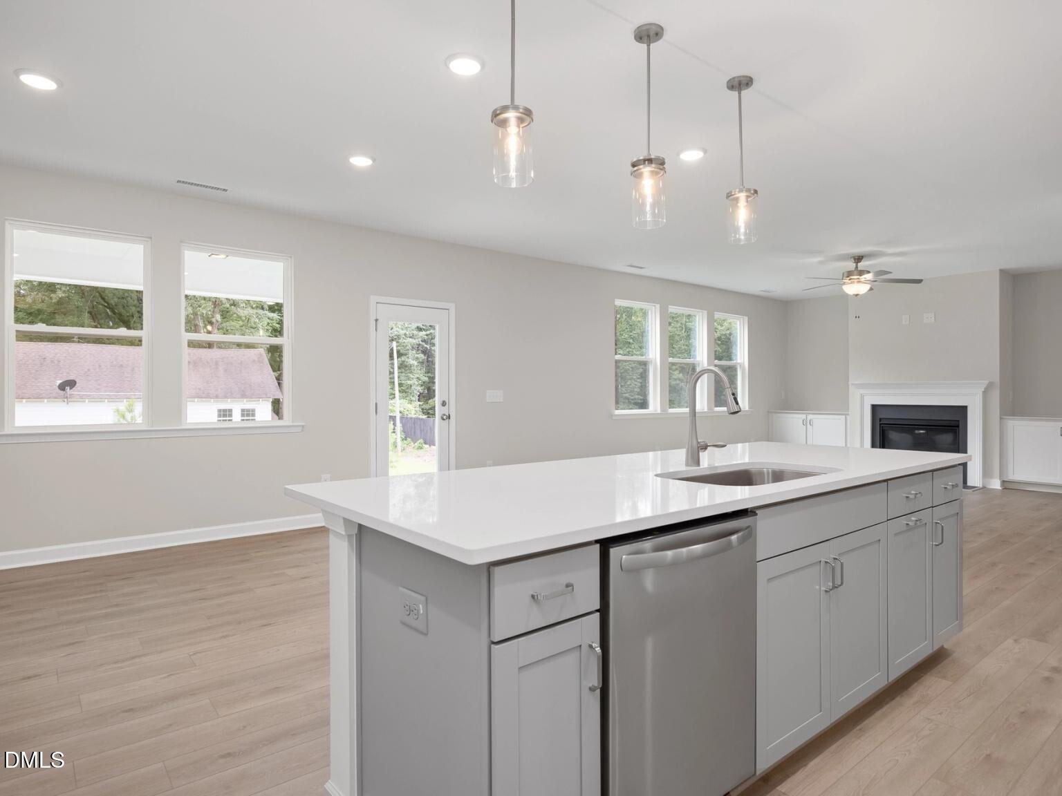 Modern open-concept kitchen with white quartz island, gray cabinets, pendant lights, and adjacent fireplace in Davidson Homes The Beech B, Wake Forest, NC