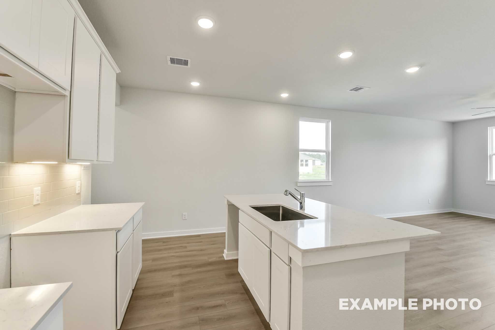 Bright open-concept kitchen in The Colorado by Davidson Homes, featuring white cabinetry, island with sink, and vinyl flooring.