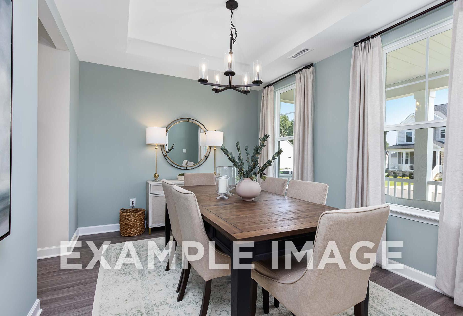Spacious dining room in The Willow E with wooden table, beige upholstered chairs, chandelier, round mirror, and large window, Davidson Homes Angier NC