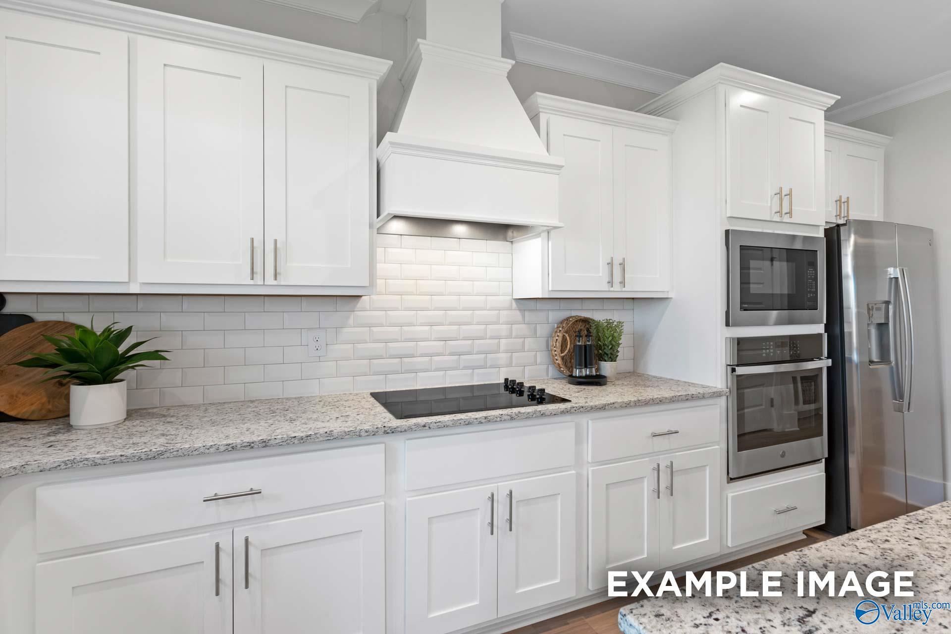 White shaker kitchen with subway tile backsplash, granite countertops, and stainless appliances in Davidson Homes Chelsea A, Toney AL