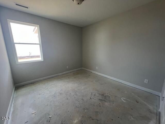Empty bedroom with light gray walls, large window, and exposed concrete floor in Davidson Homes The Adalynn B, Lillington, NC