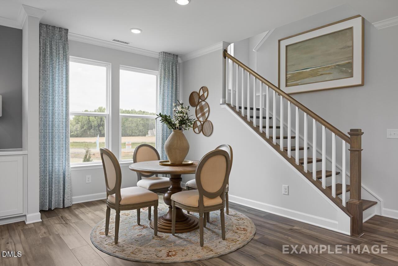 Elegant dining room with round table, upholstered chairs, large windows overlooking pond, and staircase in Davidson Homes The Magnolia B, Angier, NC