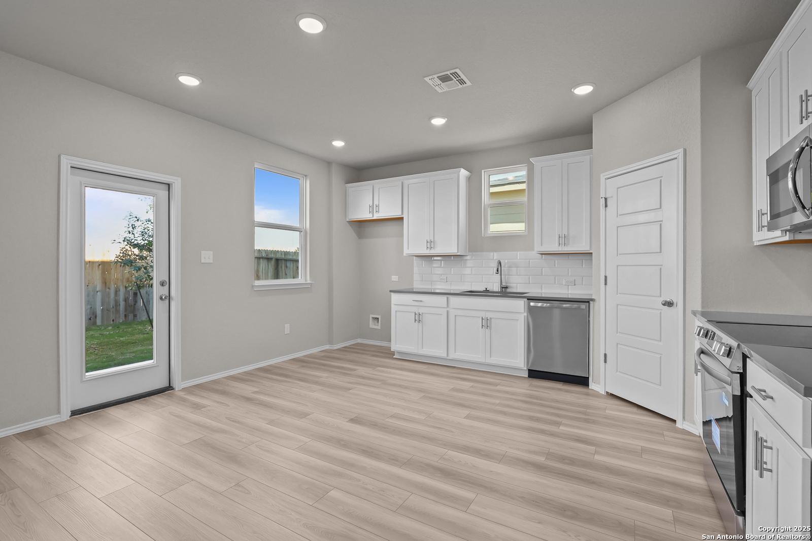 Open-concept kitchen with white shaker cabinets, stainless steel appliances, and hardwood floors in Davidson Homes The Trinity D, San Antonio