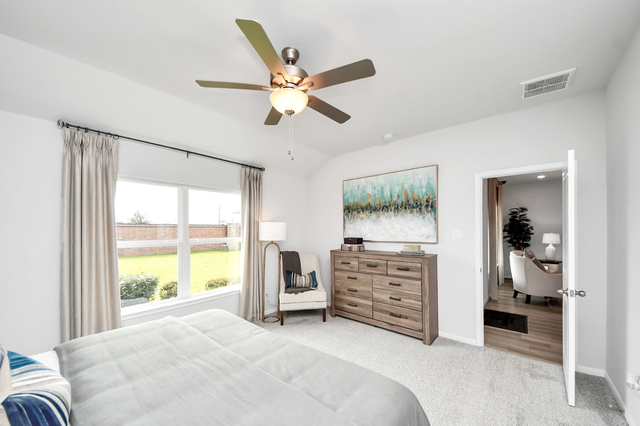 Bright bedroom in Sunterra, Katy, Texas by Davidson Homes featuring a ceiling fan, wood dresser, and view of the backyard.