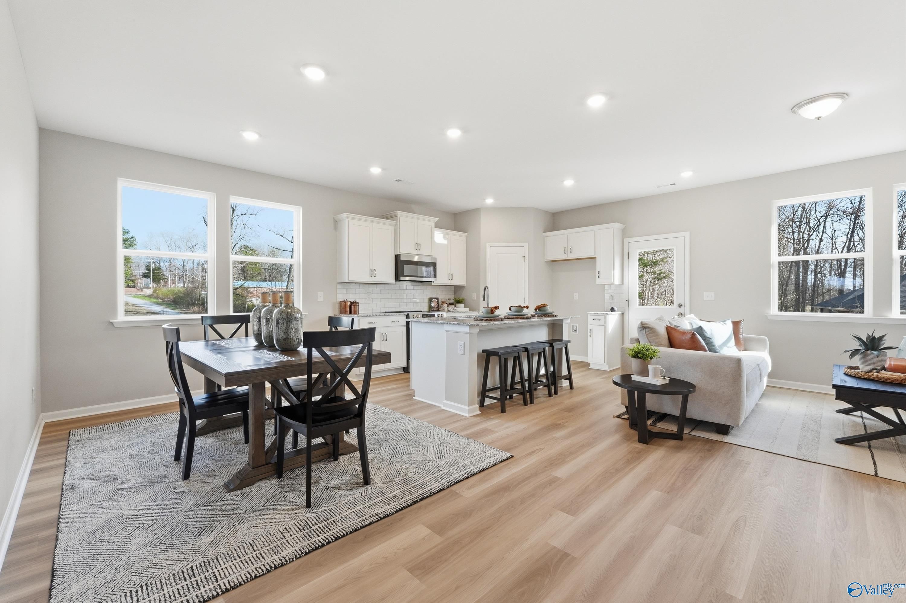 Open-concept kitchen and dining area with white cabinets, island bar stools, and hardwood floors in The Polaris 3-bedroom home, Fayetteville, Tennessee