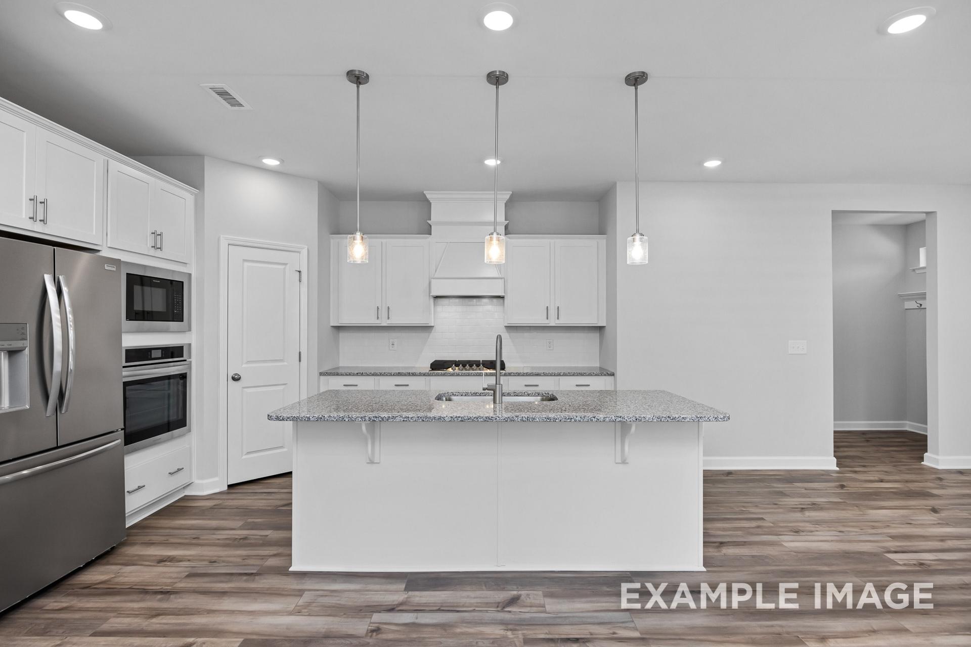 Modern kitchen in The Preston B showcasing white shaker cabinets, granite island, stainless steel appliances, pendant lights