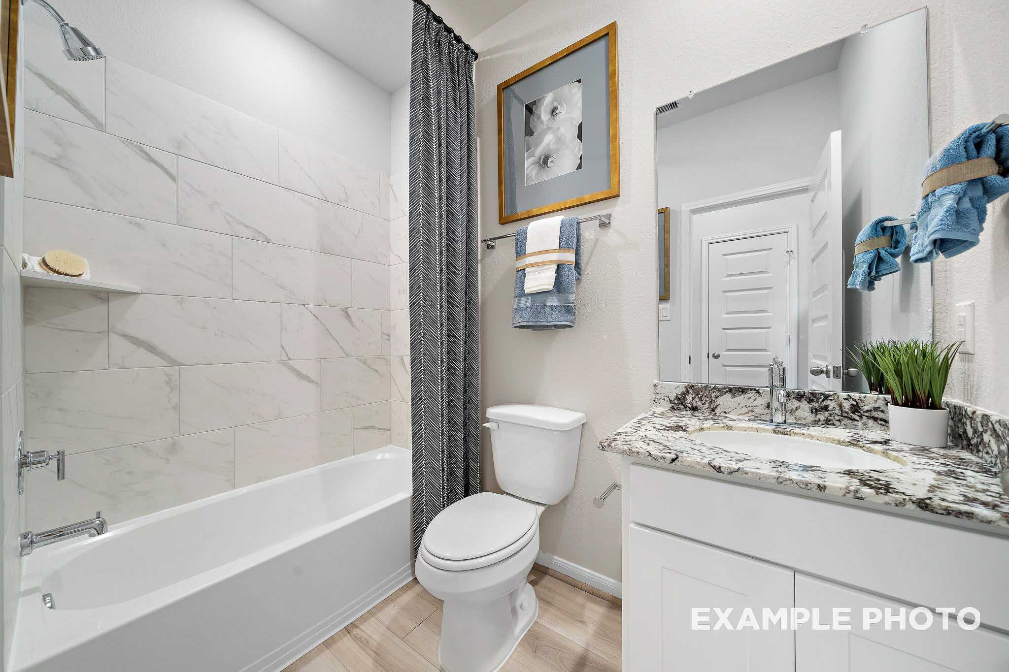 Spacious master bathroom in The San Marcos B with white subway tile tub-shower, quartz vanity, blue towels, and potted plant