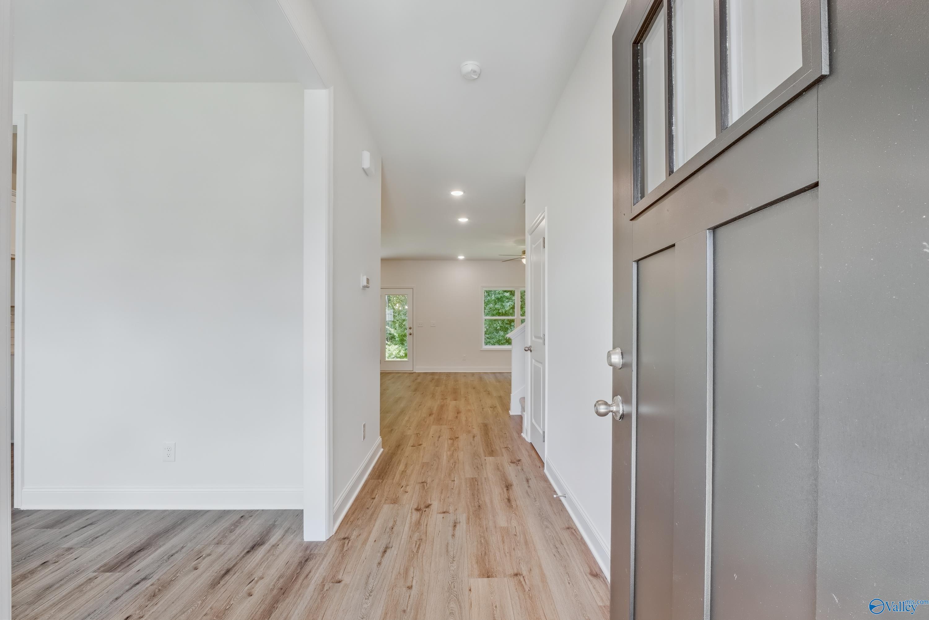 Bright entry hallway with hardwood floors, white walls, and glass-paneled front door in Davidson Homes The Shelby A, Arab, Alabama
