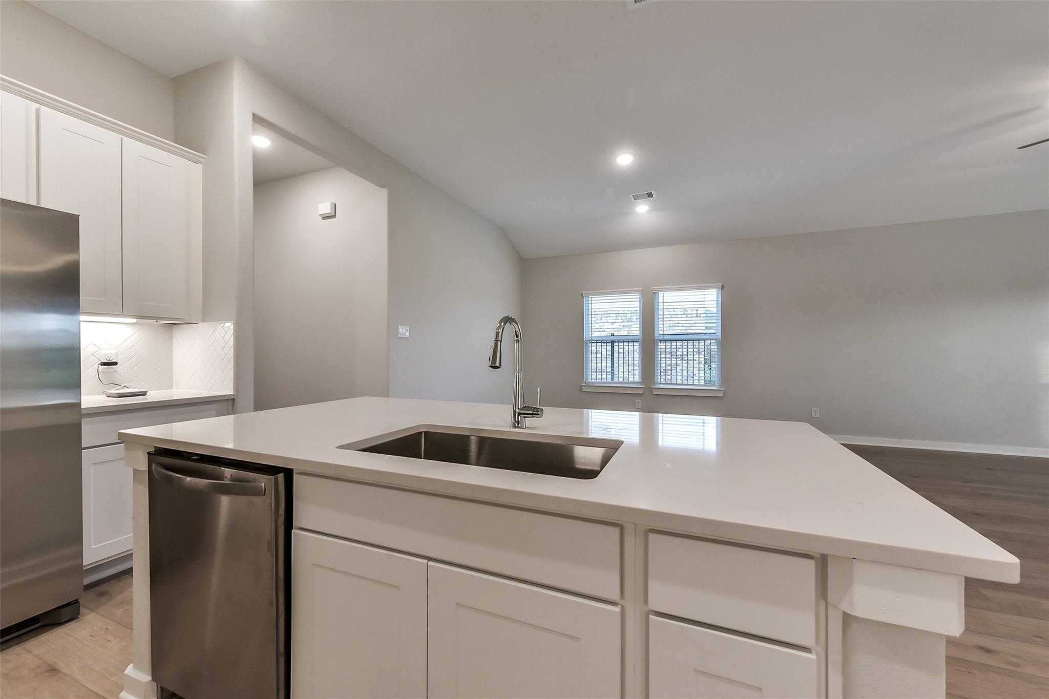 Modern white kitchen island with stainless sink, dishwasher, and cabinets in open-concept layout, Davidson Homes The Laguna B, Katy, Texas