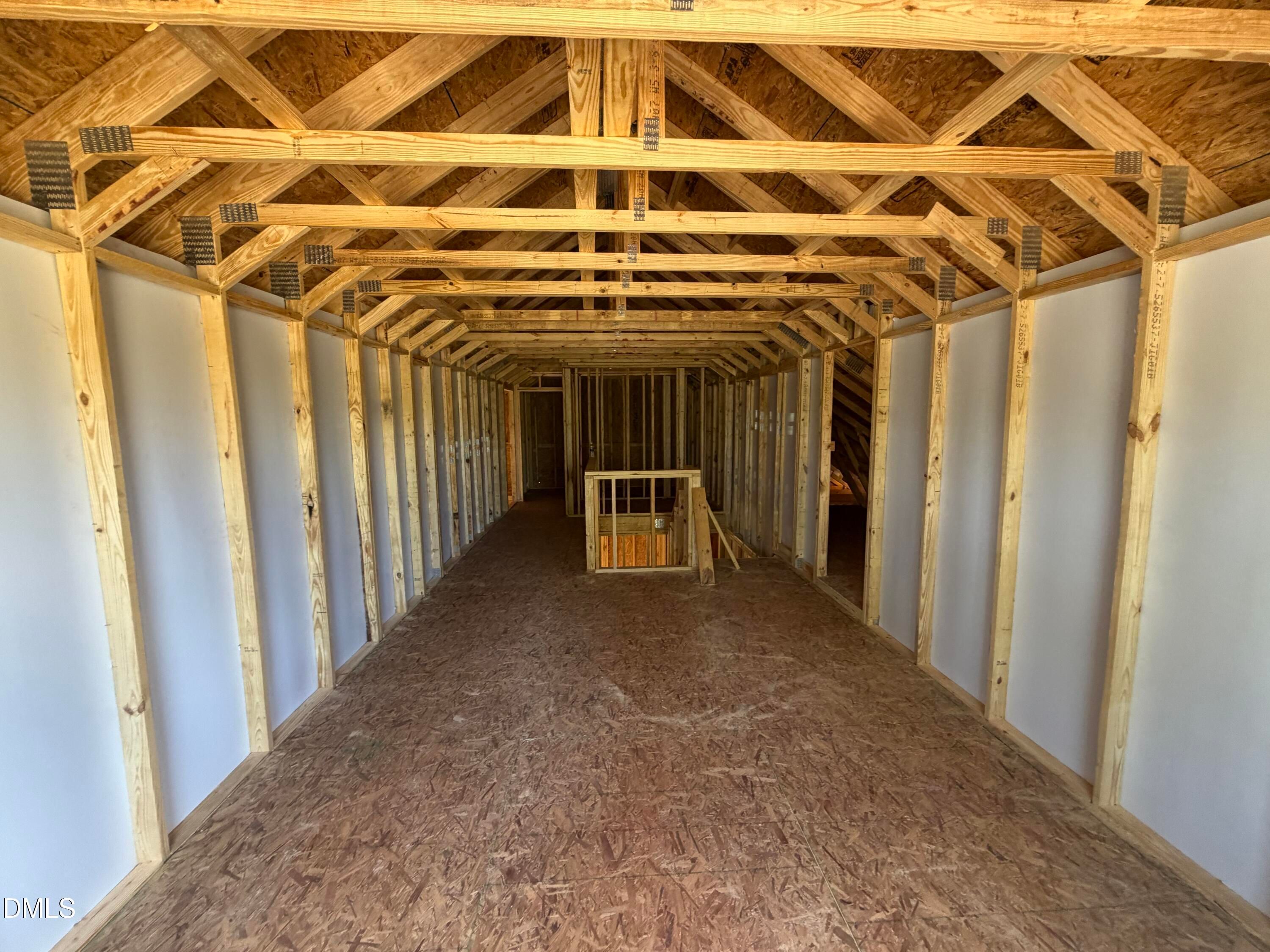 Spacious unfinished garage interior with exposed wooden trusses and plywood walls in 4-bedroom Hickory II C home, Lillington NC