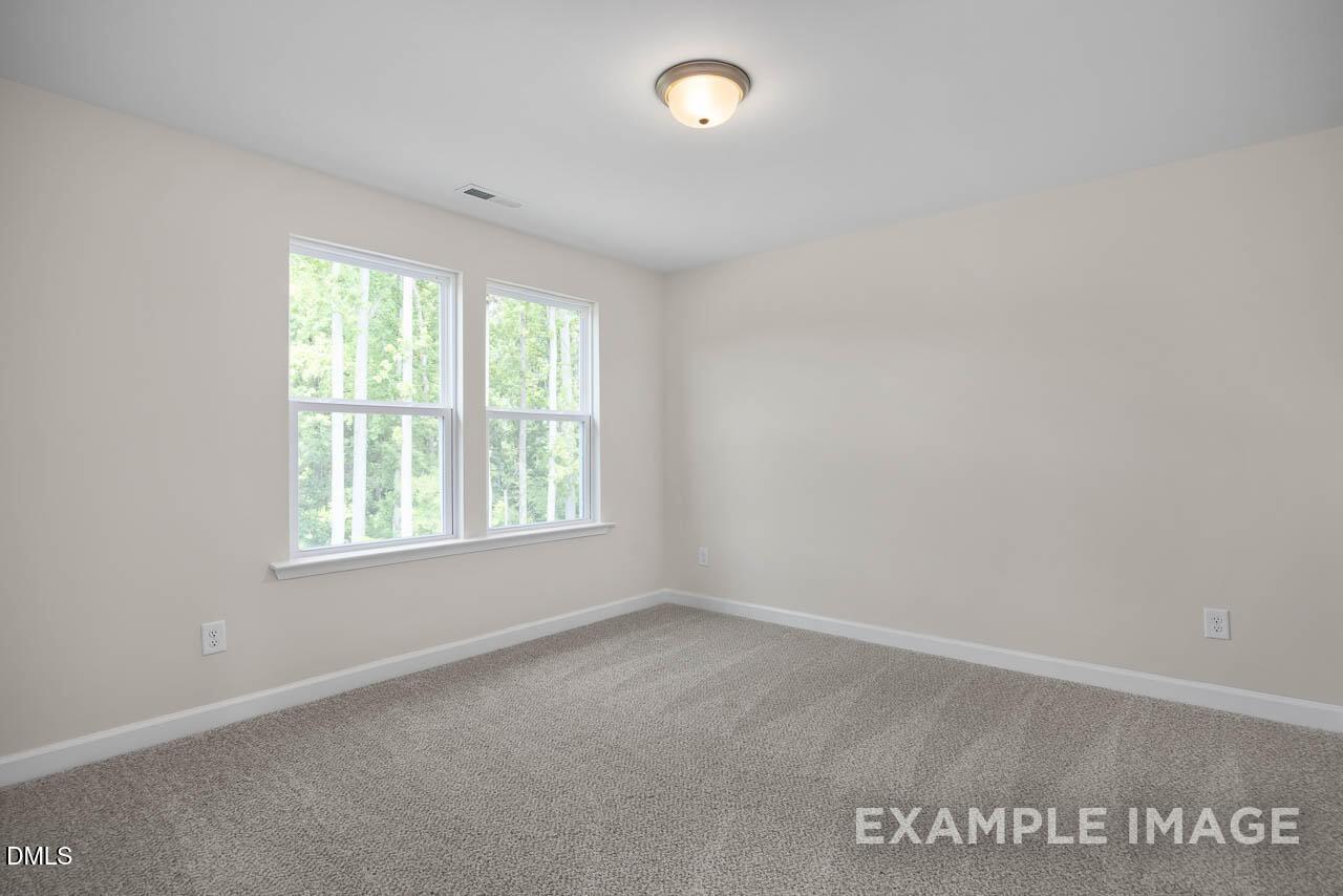 Bright empty bedroom with large windows, natural light, beige walls, and gray carpet in The Willow D floor plan, Lillington, NC