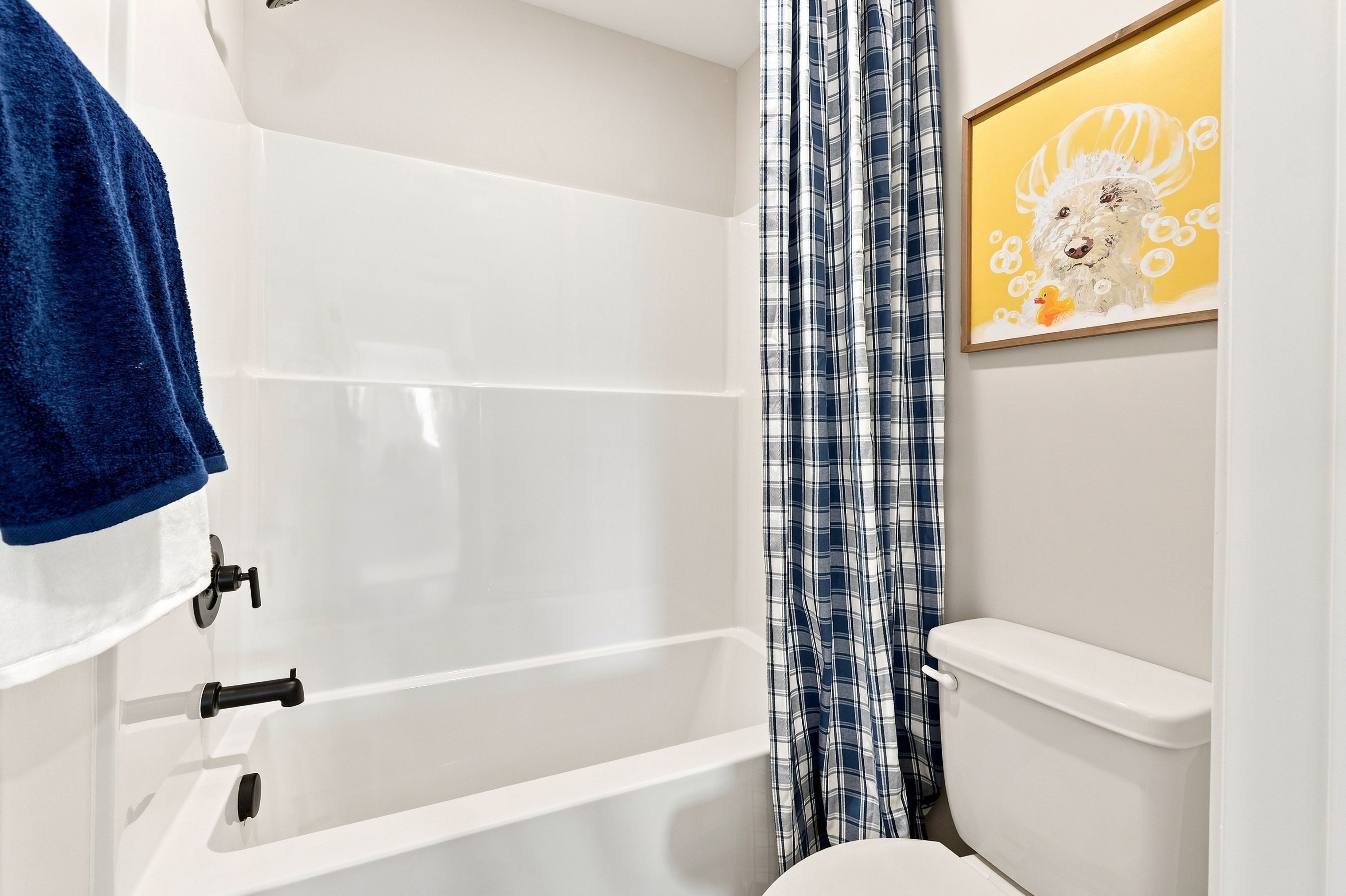 White bathtub with black fixtures, blue plaid shower curtain, and toilet in a bathroom at Bailey Park by Davidson Homes in Fayetteville, TN