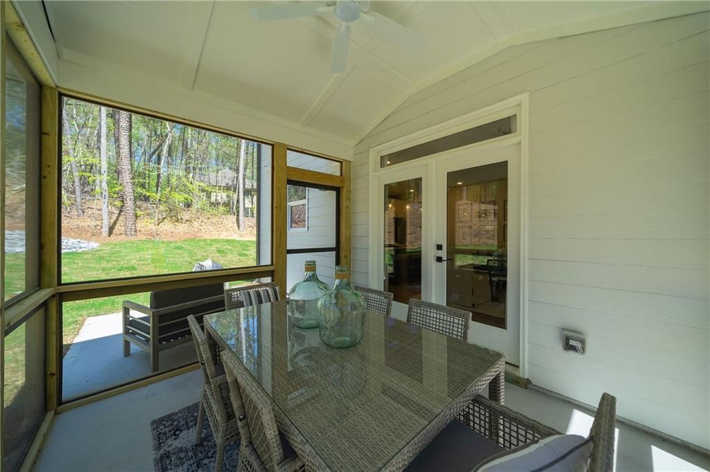Screened porch with glass-top dining table, wicker chairs, ceiling fan overlooking wooded backyard in Davidson Homes The Willow B, Riverwood, GA
