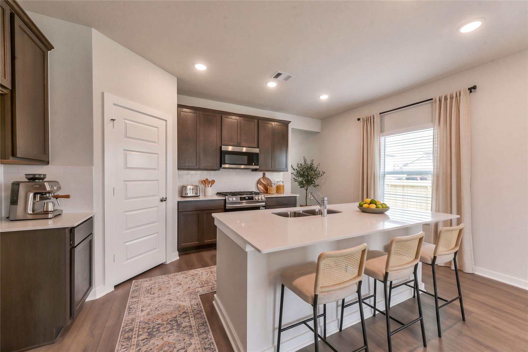 Modern kitchen with quartz island, dark cabinets, stainless appliances, bar stools in Davidson Homes Sabine F, Dayton TX