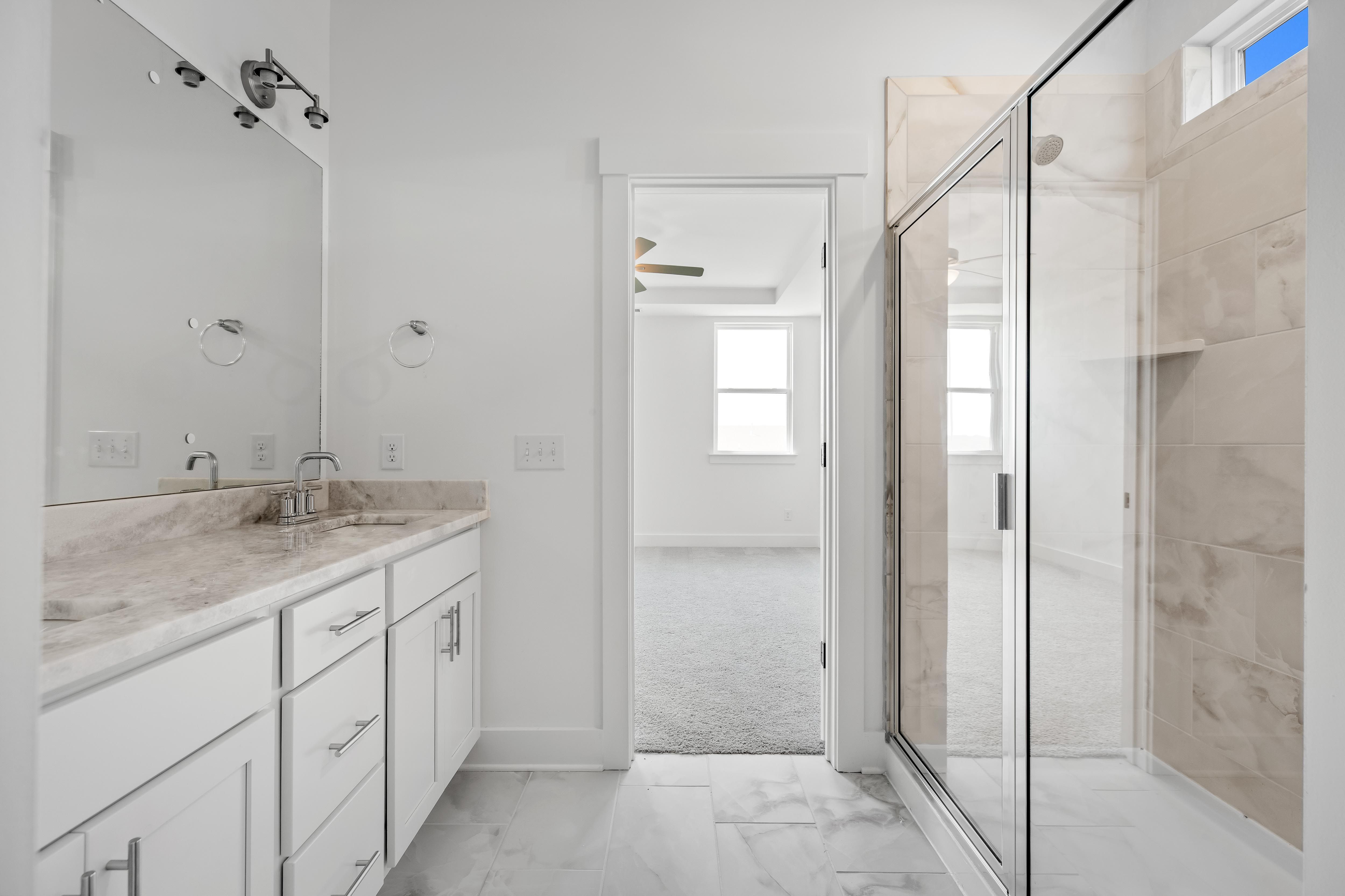 Modern master bathroom in The Cedar D with white vanity, marble-style countertops, and a glass-enclosed walk-in shower.
