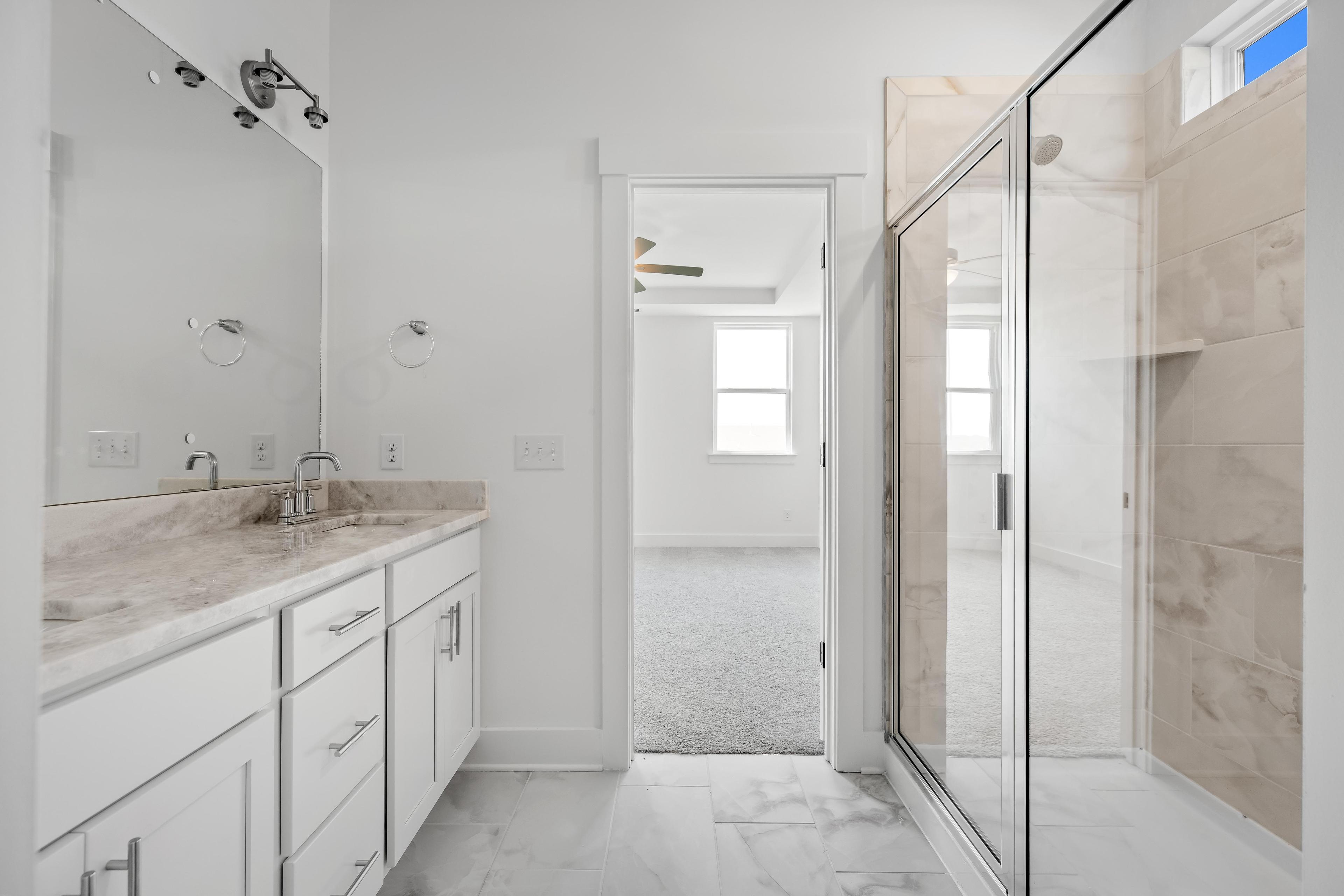 Modern master bathroom in The Cedar D with white vanity, marble-style countertops, and a glass-enclosed walk-in shower.