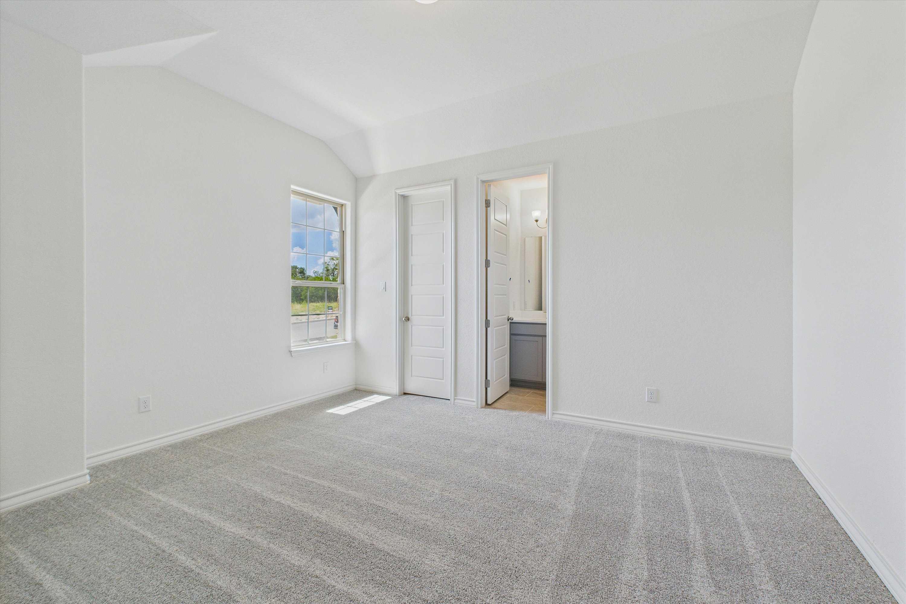 Spacious secondary bedroom with en-suite bath, carpeted floor, and large window in Davidson Homes The Summerlin C, Castroville, Texas