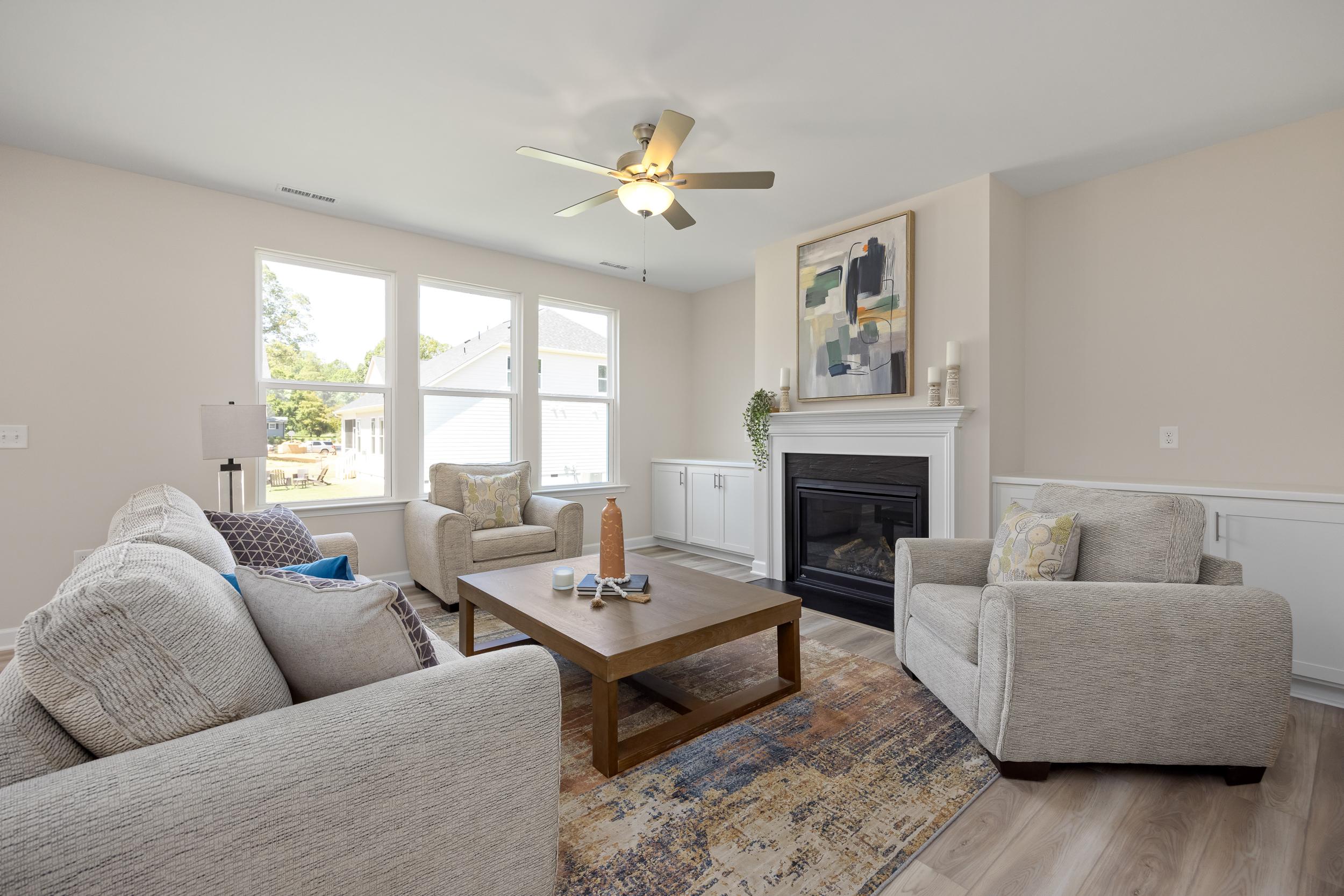 Cozy living room in Montrose Aberdeen NC featuring gas fireplace, beige sofas, coffee table, ceiling fan and hardwood floors by Davidson Homes