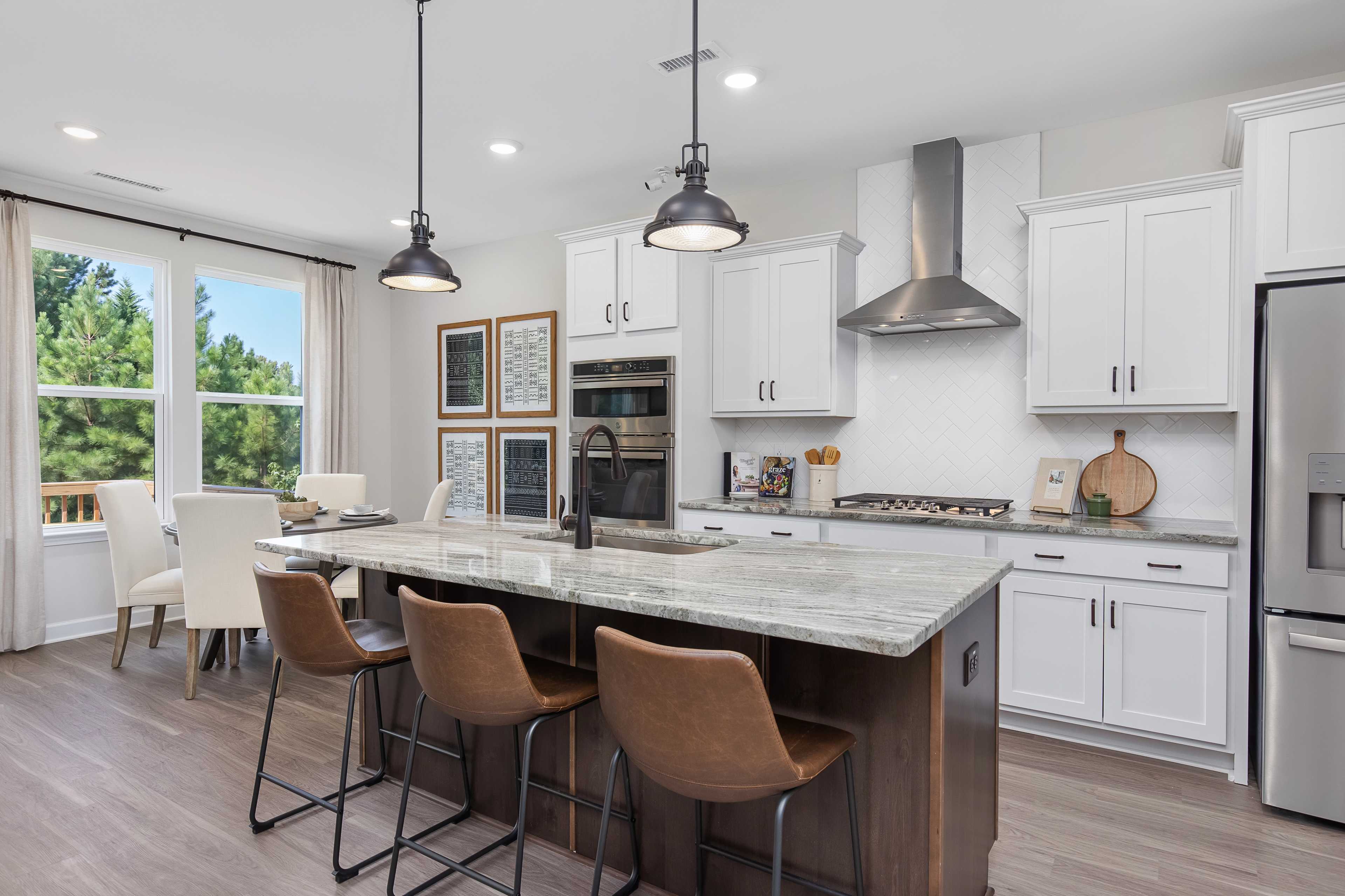 Modern kitchen at Woodland Crossing in Zebulon NC with white cabinets, quartz island, leather stools, stainless appliances, and hardwood floors