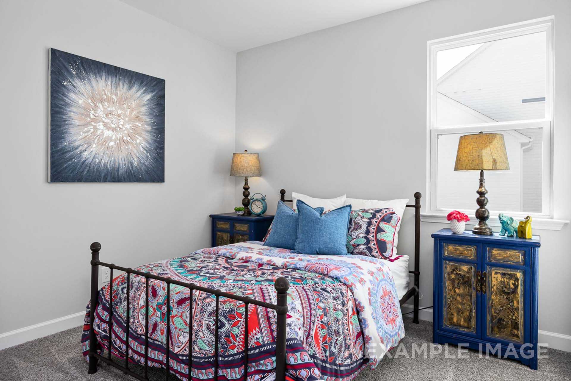 Cozy secondary bedroom in The Carter B with iron frame bed, colorful patterned bedding, abstract wall art, and bedside lamps