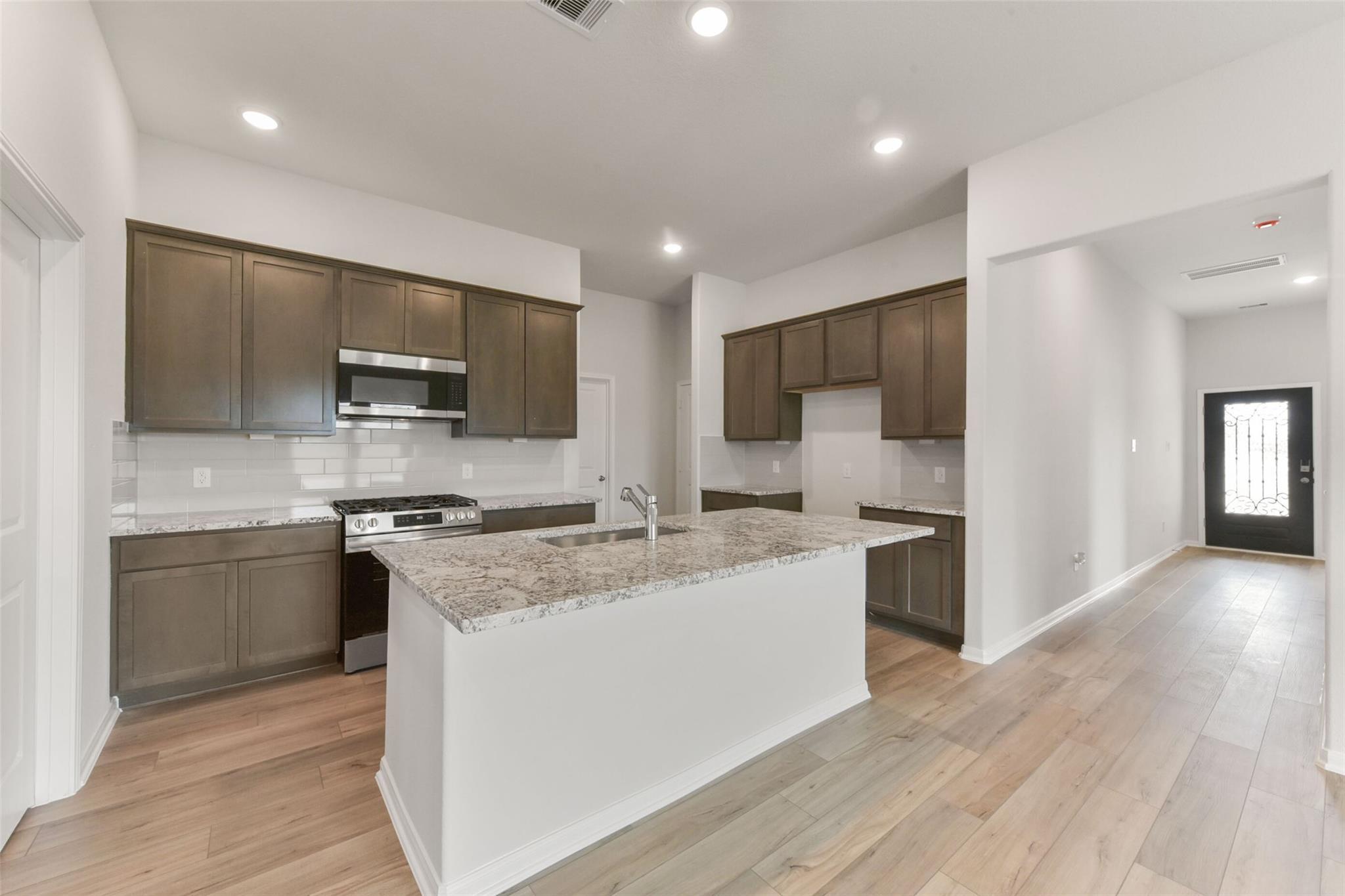 Modern kitchen with warm shaker cabinets, granite island sink, stainless appliances in The Laguna B home, Magnolia, Texas