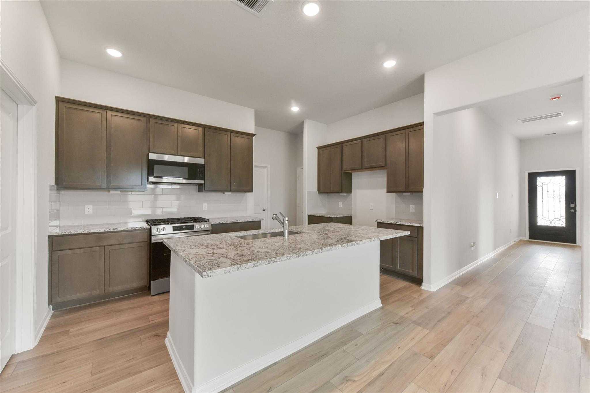 Modern kitchen with shaker cabinets, granite island sink, stainless appliances in Davidson Homes The Laguna B, Magnolia Texas