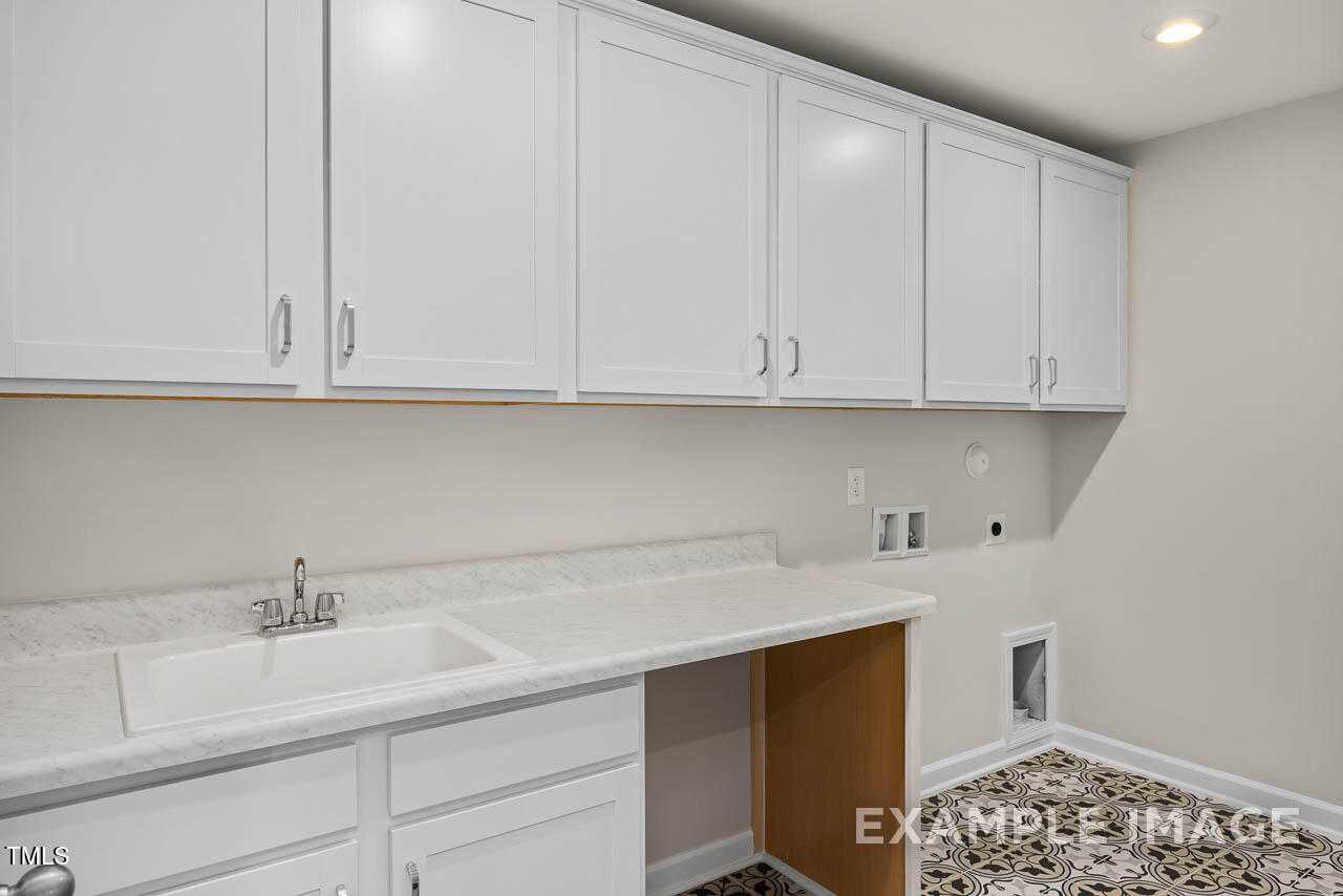 Modern laundry room with white shaker cabinets, quartz countertop, sink, and pet door in The Hickory II B by Davidson Homes, Lillington, NC